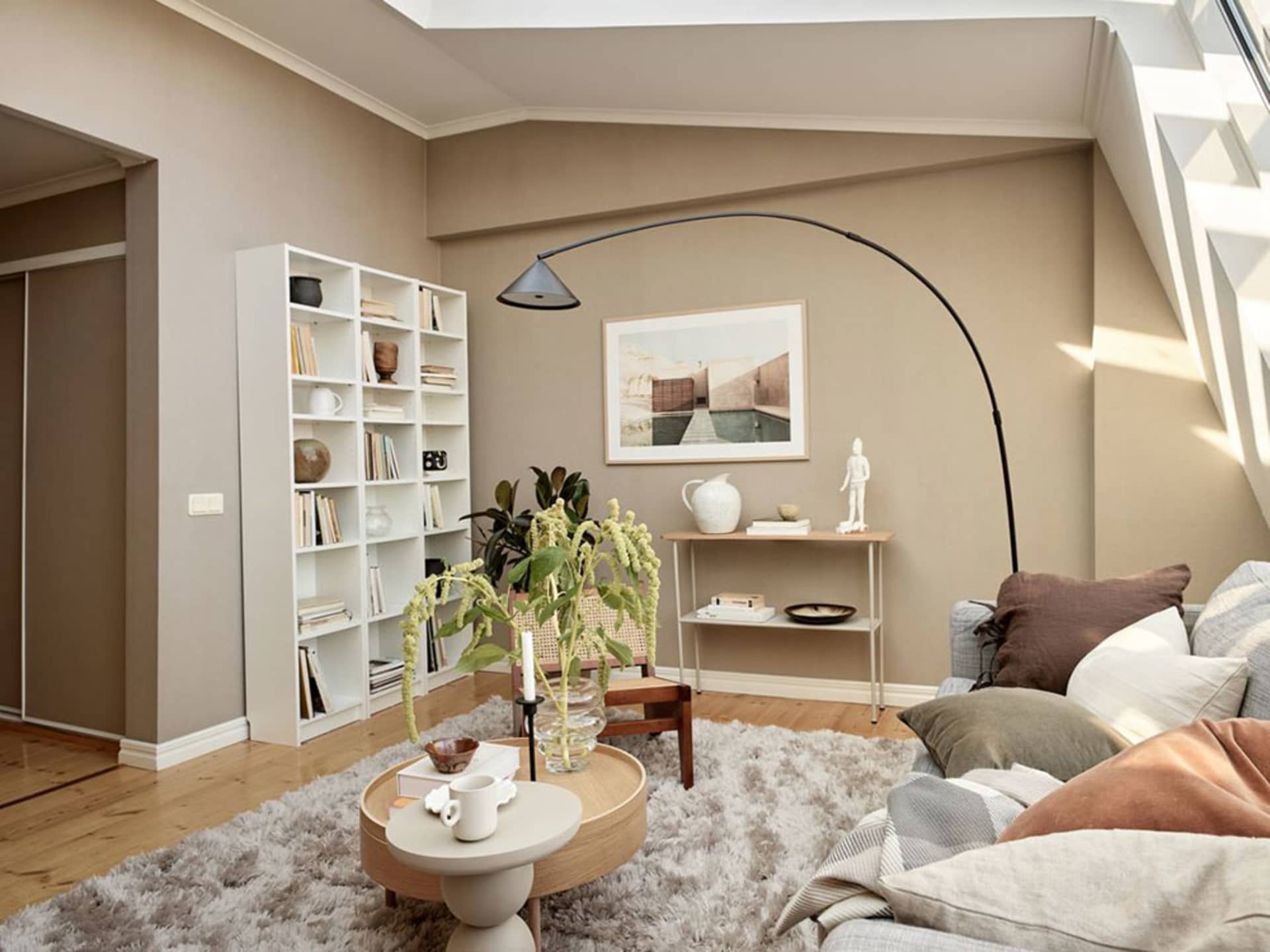 Minimalist living room with concrete and wooden elements, round table, white shelves, and floor lamp.