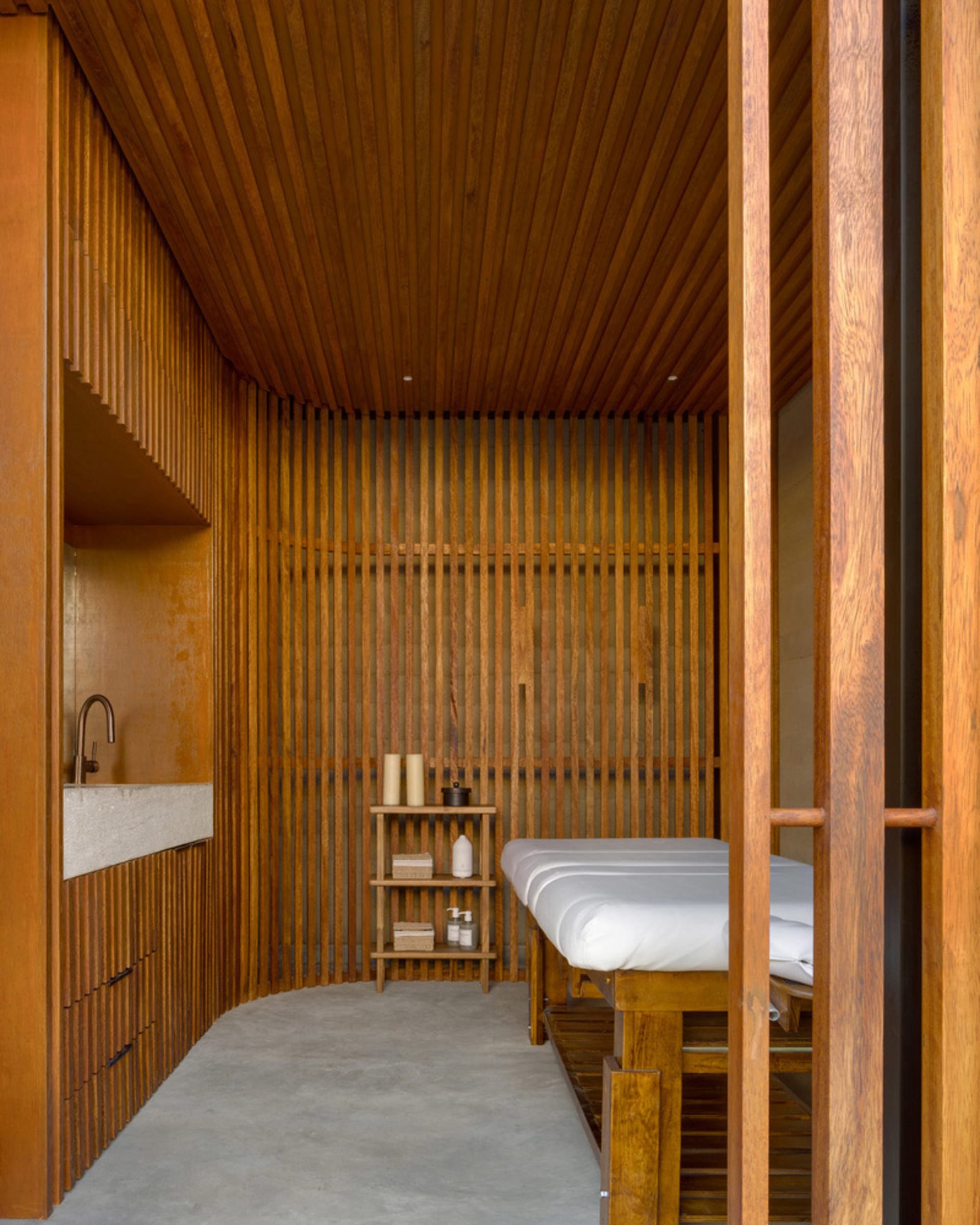 Minimalist spa room with wooden walls and ceiling, concrete floor, and massage table.