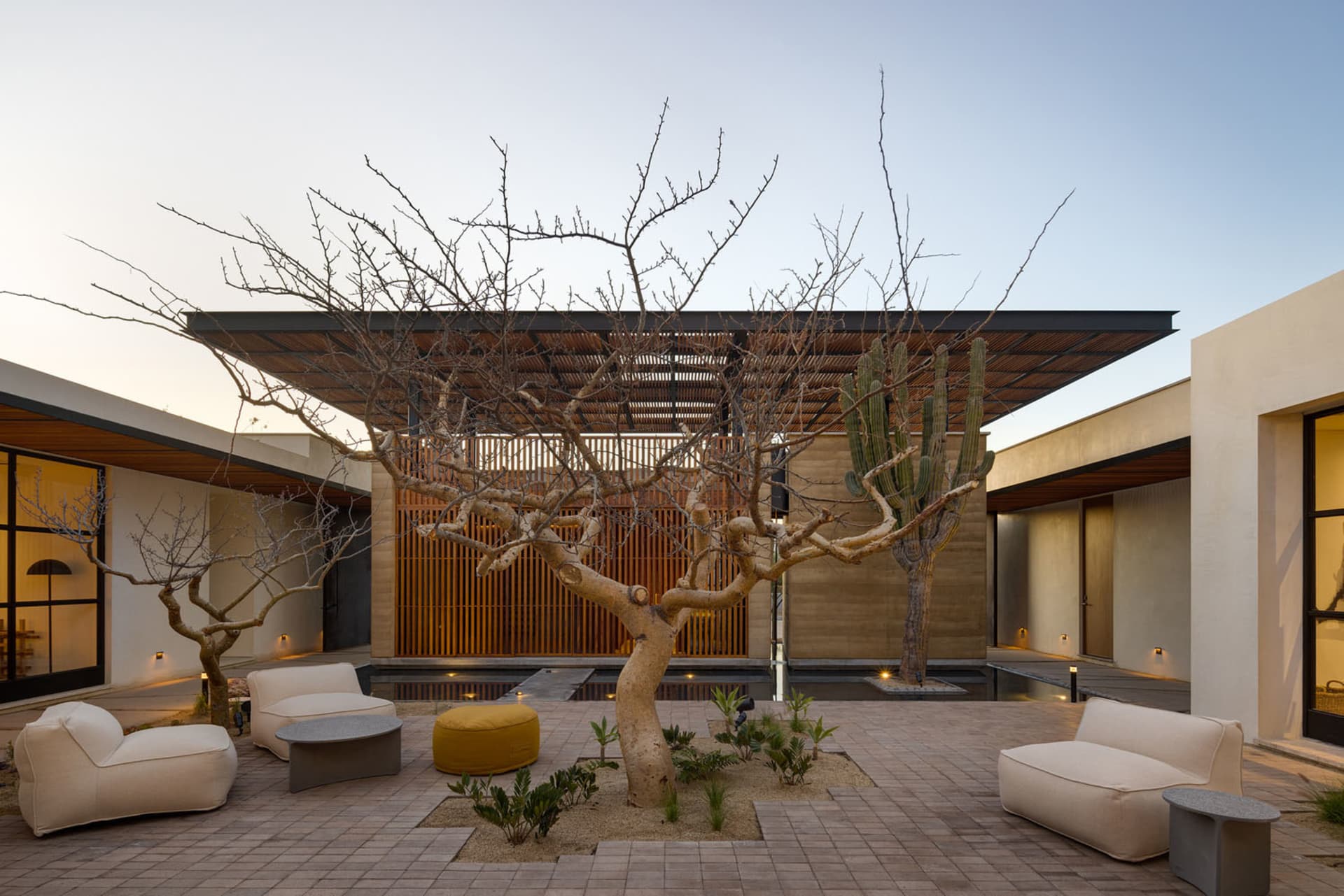 A modern garden lounge featuring concrete furniture, canvas seating, and matte lighting fixtures.