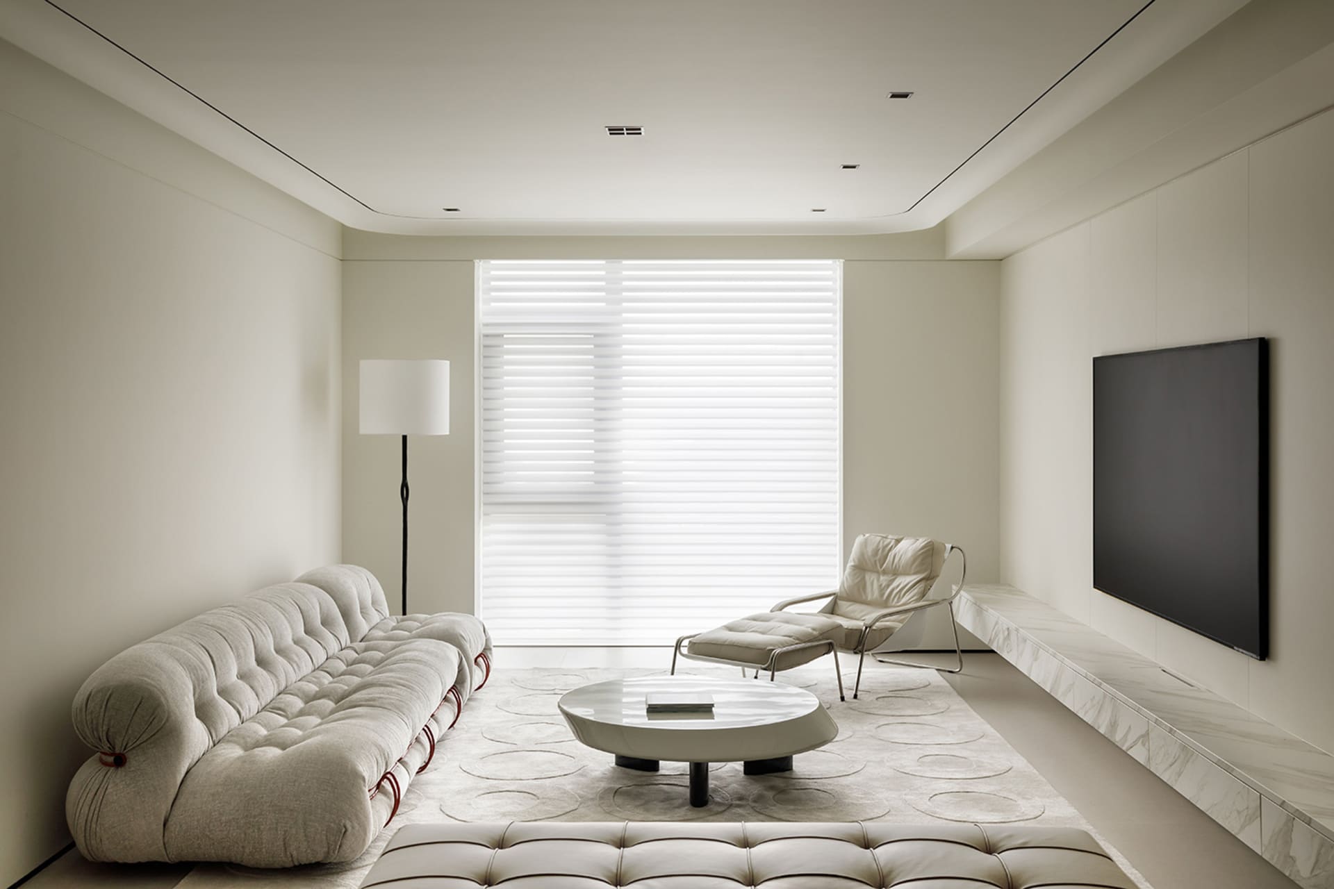 Modern living room with a white sofa, chaise lounge, round coffee table, and marble flooring.