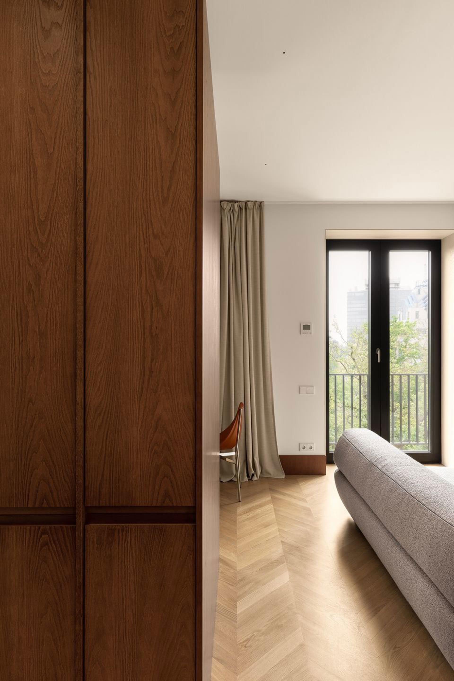 A modern living room featuring a wooden cabinet, a glass door leading to a balcony, and a gray fabric sofa.