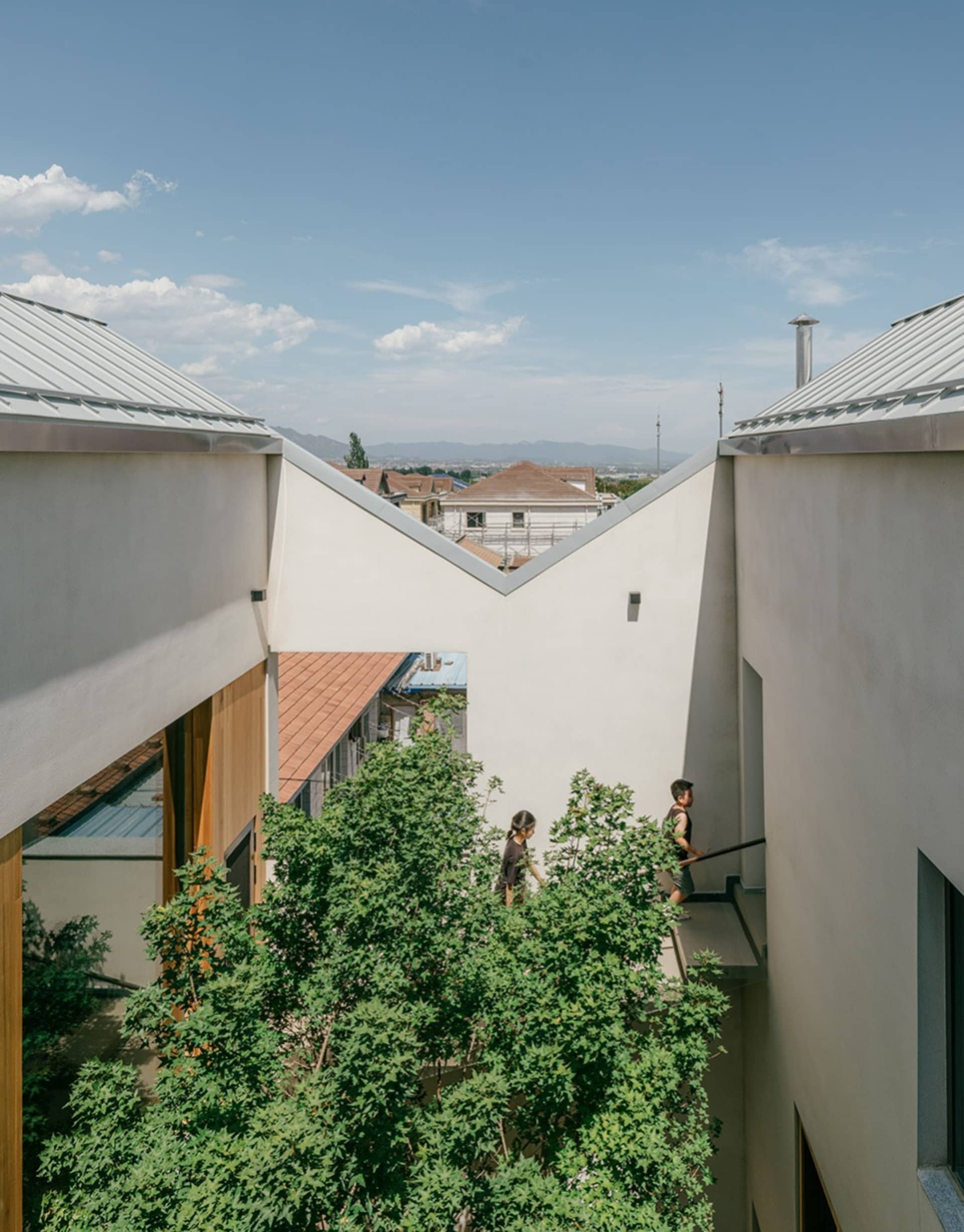 A modern residential house with a concrete exterior, set against a backdrop of greenery and distant mountains.