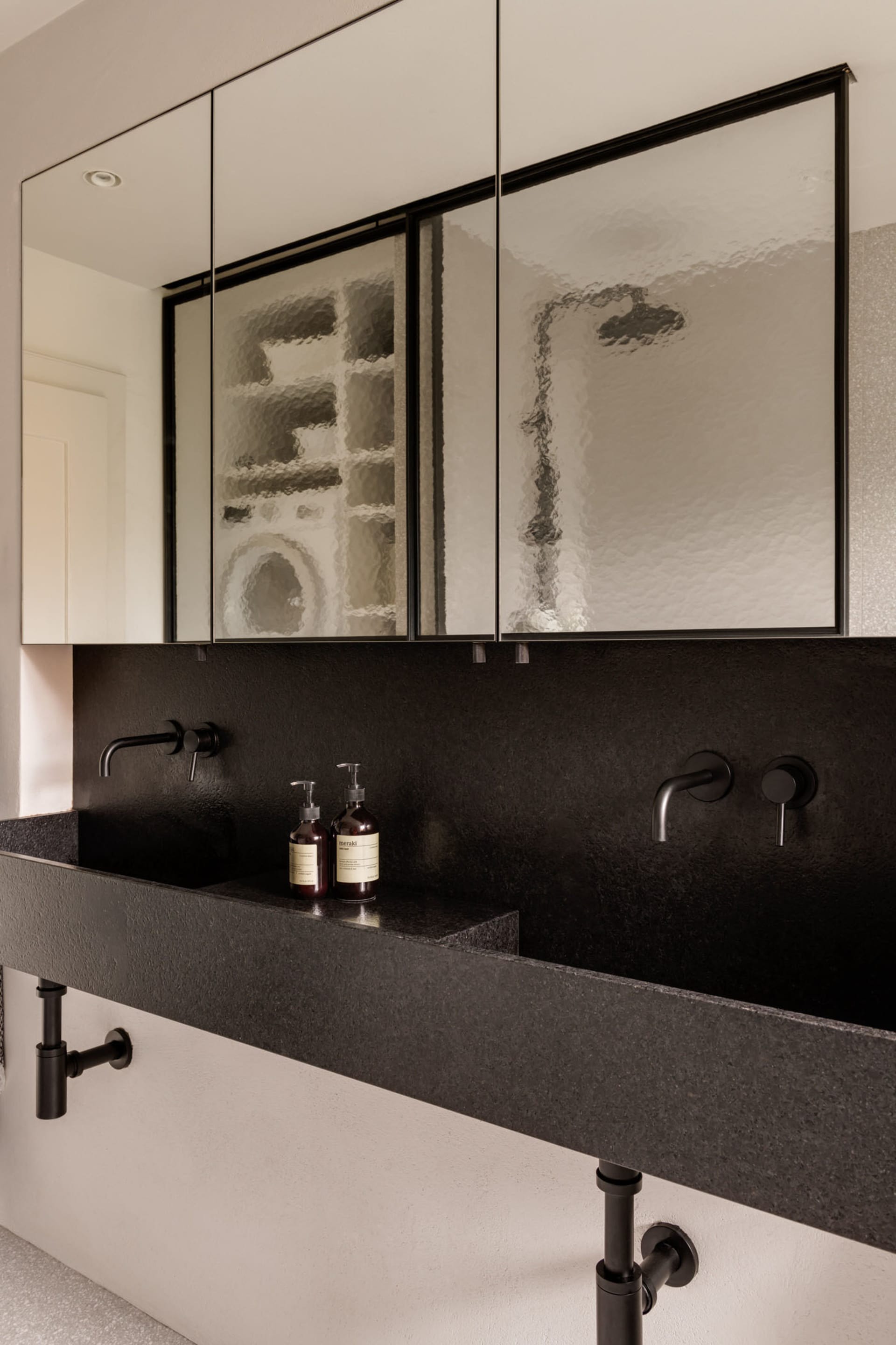 A modern bathroom interior featuring a black concrete countertop sink, dark tiles, and a minimalist design.