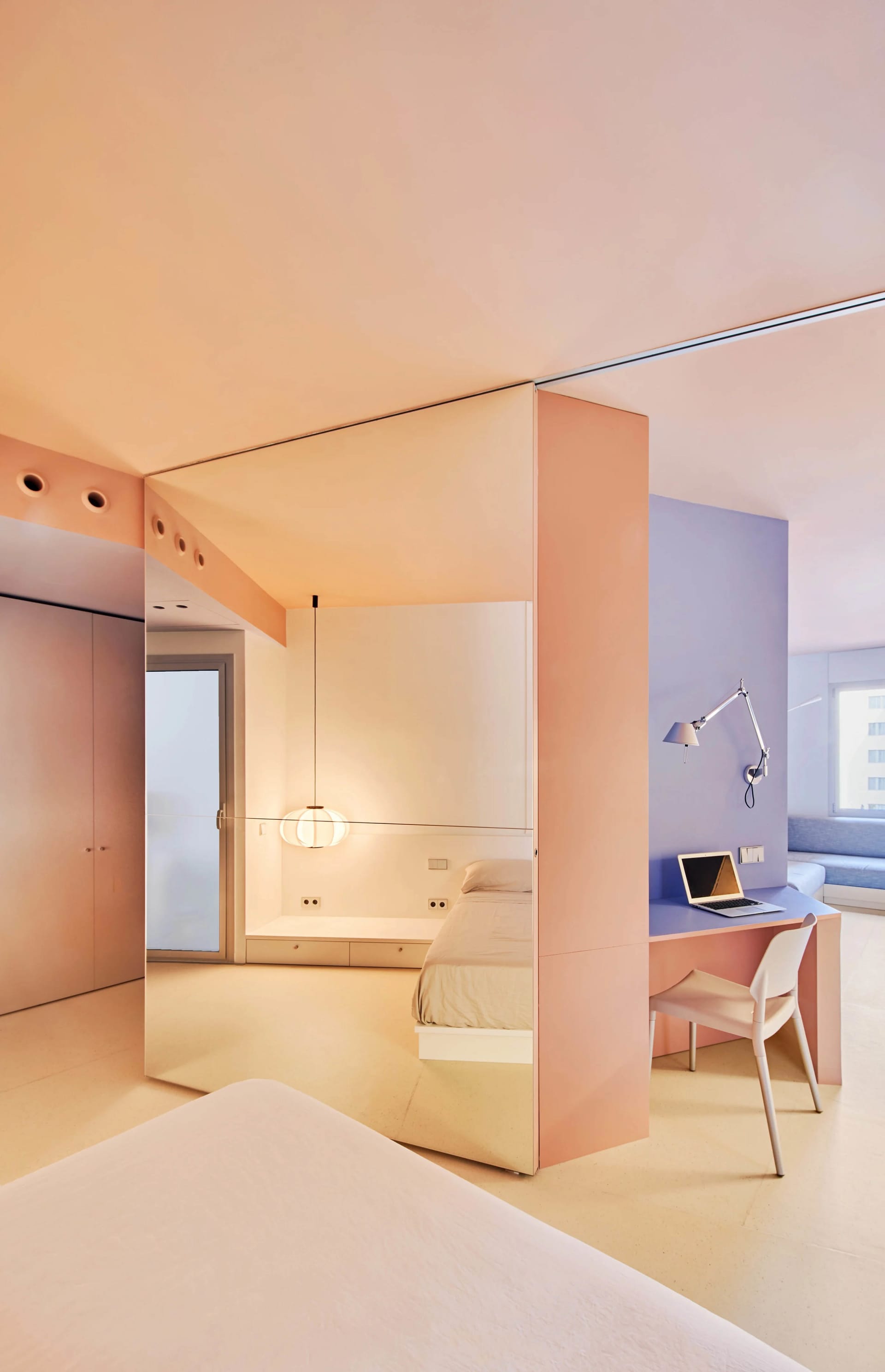 Minimalist bedroom with pink and white walls, a bed, and a desk with a laptop.