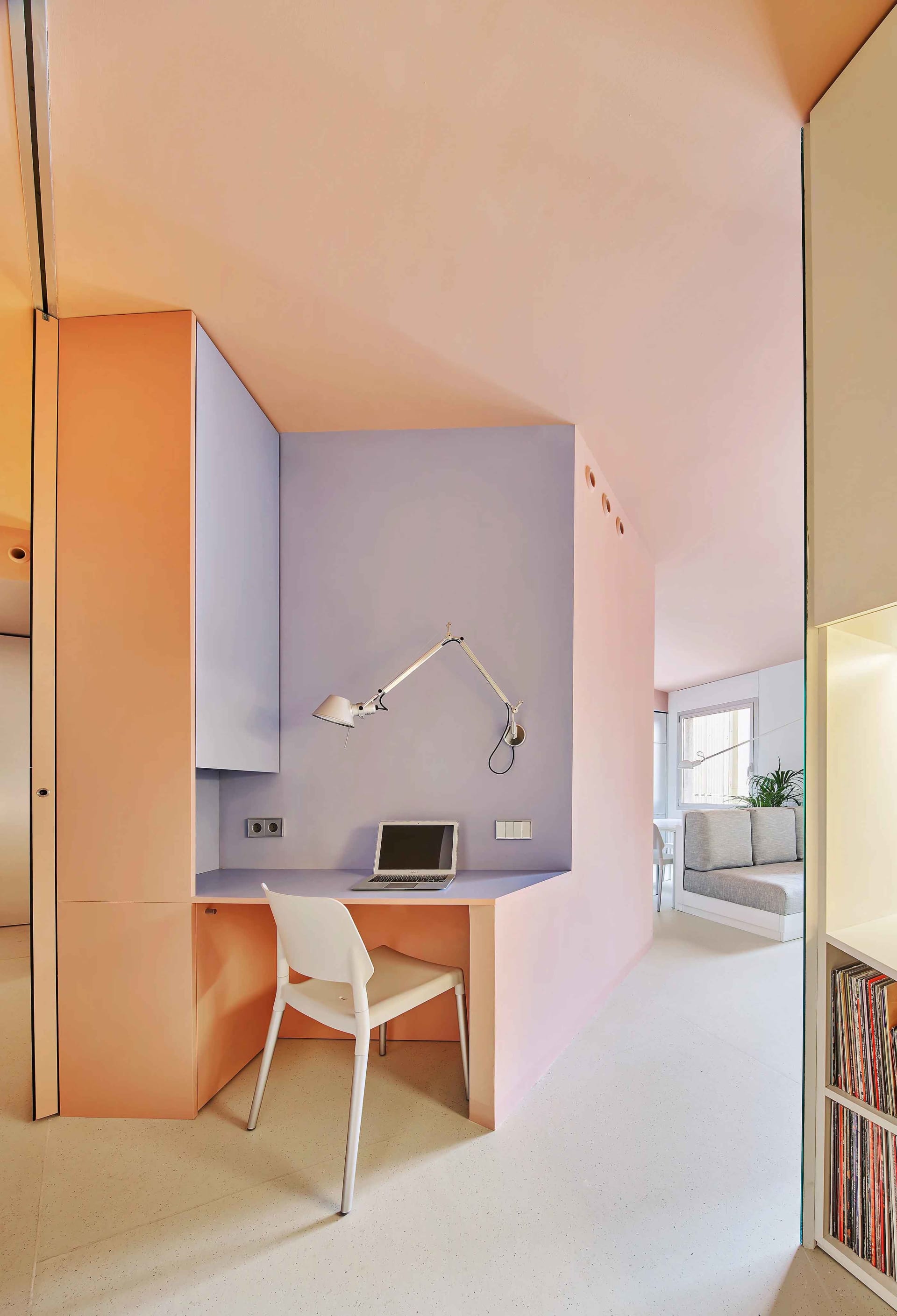 A modern home office featuring a desk with a laptop and lamp, surrounded by pastel-colored walls.