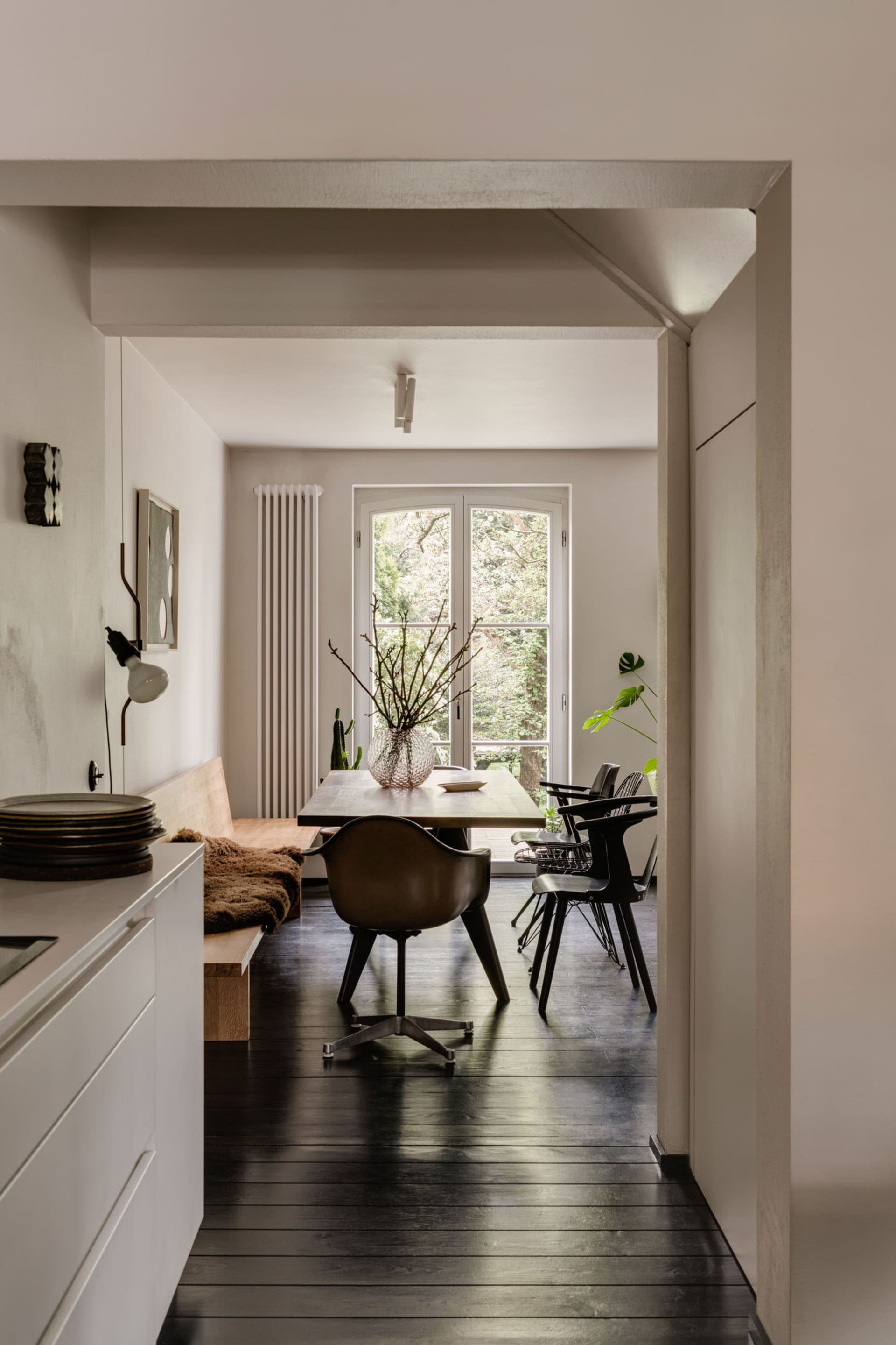 Modern dining room with transparent vase on wooden table, black chairs, and glass windows showcasing trees.