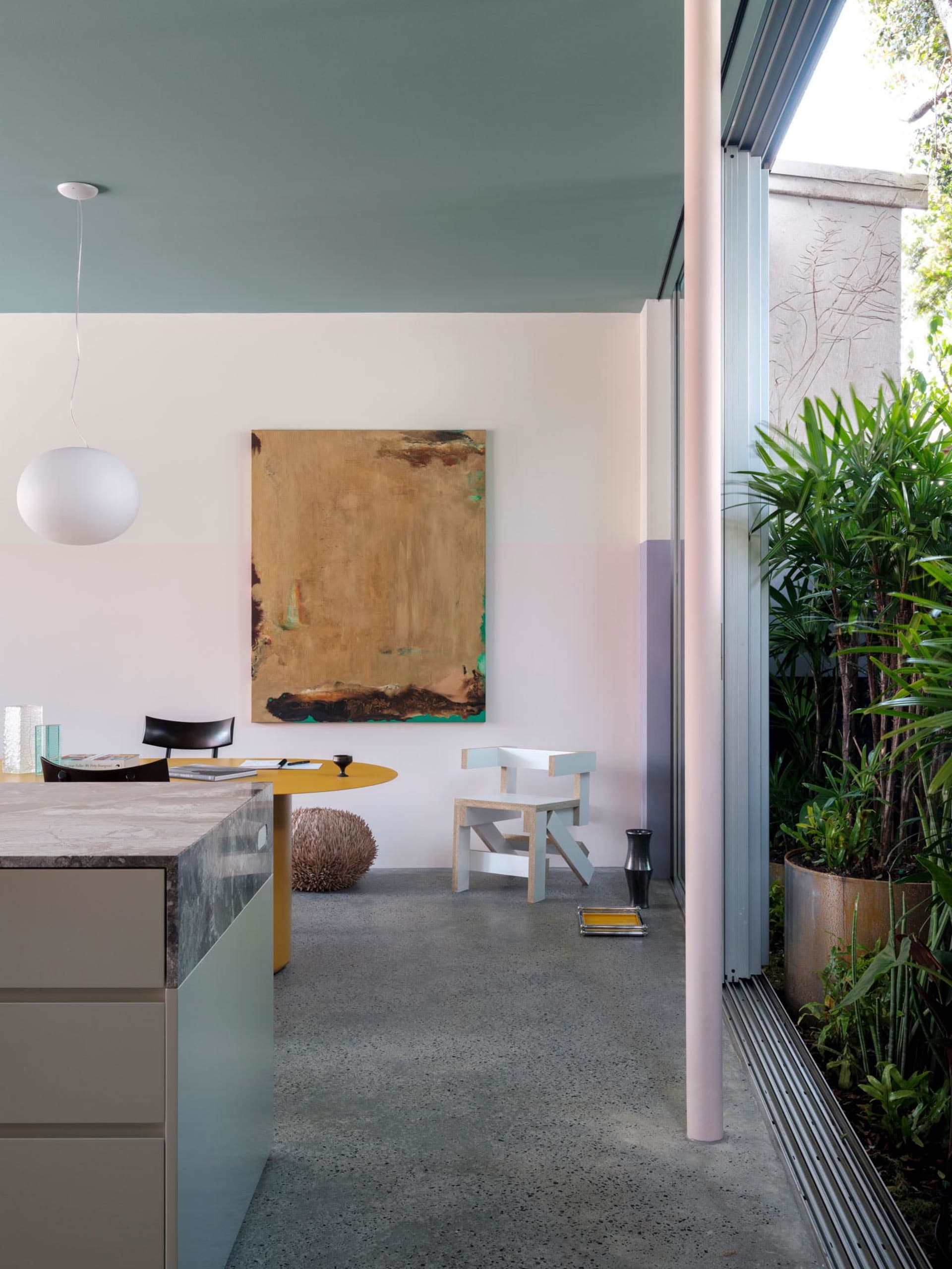 A minimalist residential kitchen with a concrete floor, concrete countertop, and a large abstract painting.
