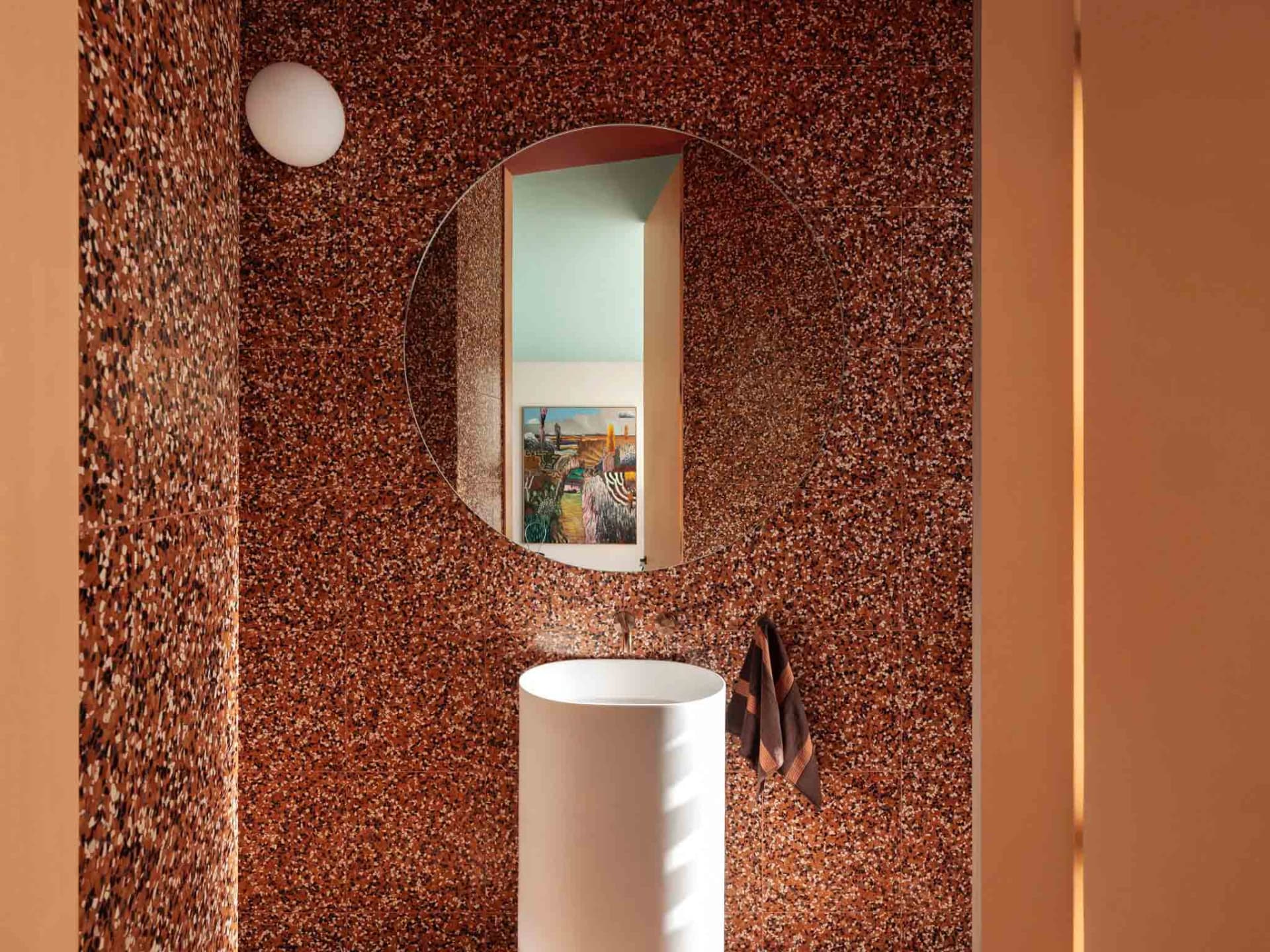 A modern bathroom features walls with a speckled granite texture and a cylindrical white pedestal sink.