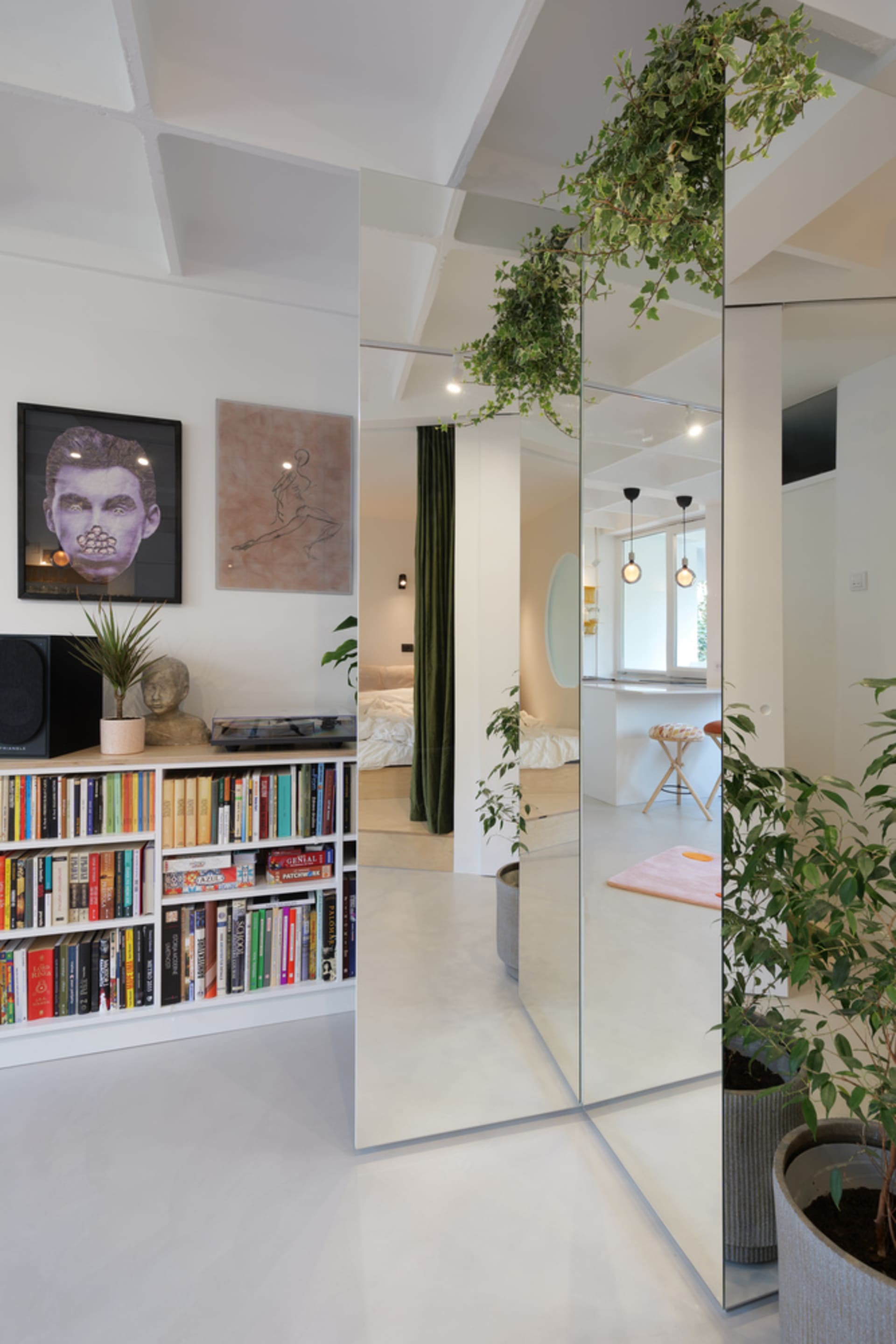 A modern white living space featuring glass walls, a green plant, and a white floor, with a white bookshelf filled with books