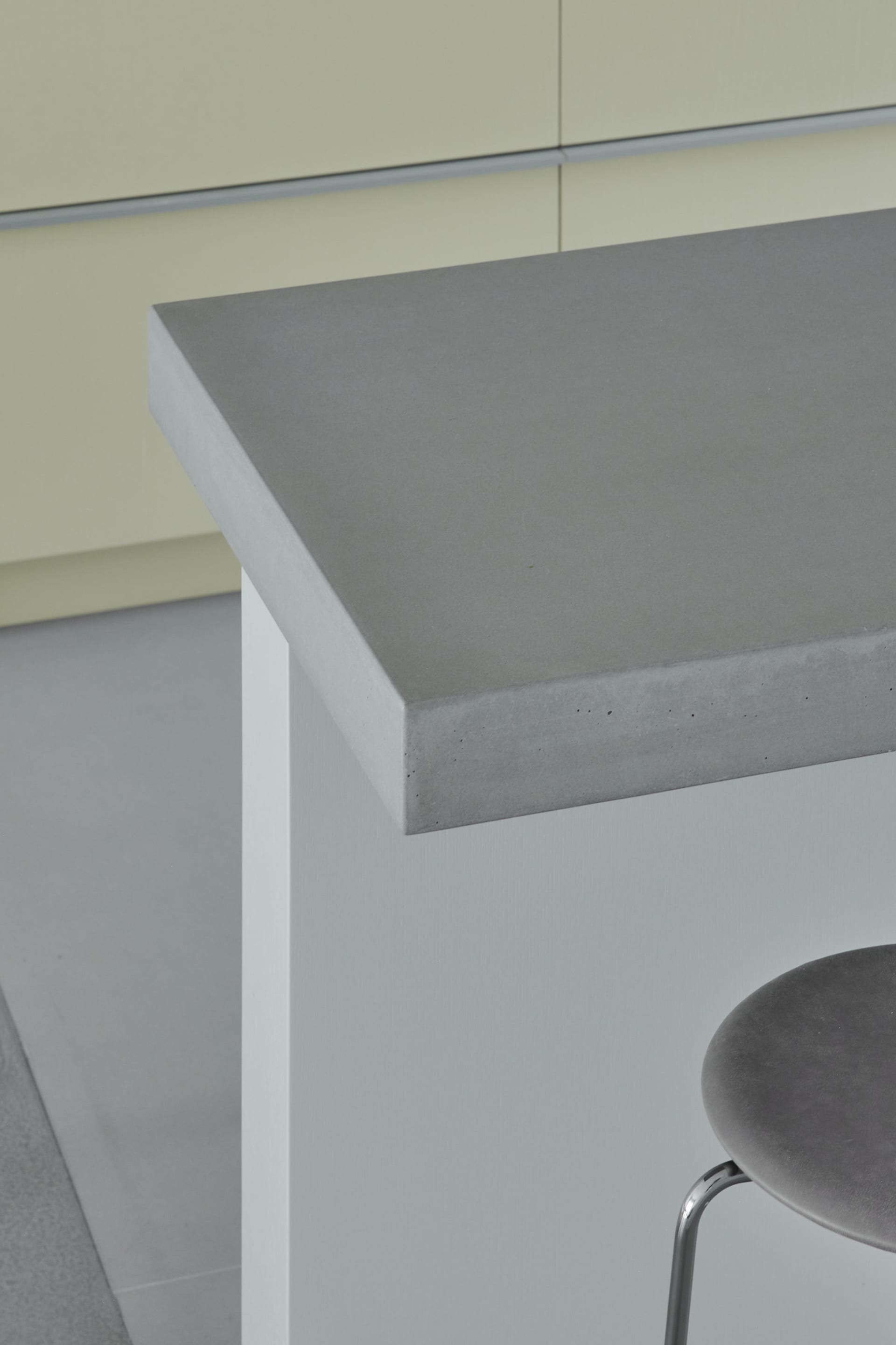 A modern, minimalist kitchen with a grey concrete countertop and sleek, white cabinets.