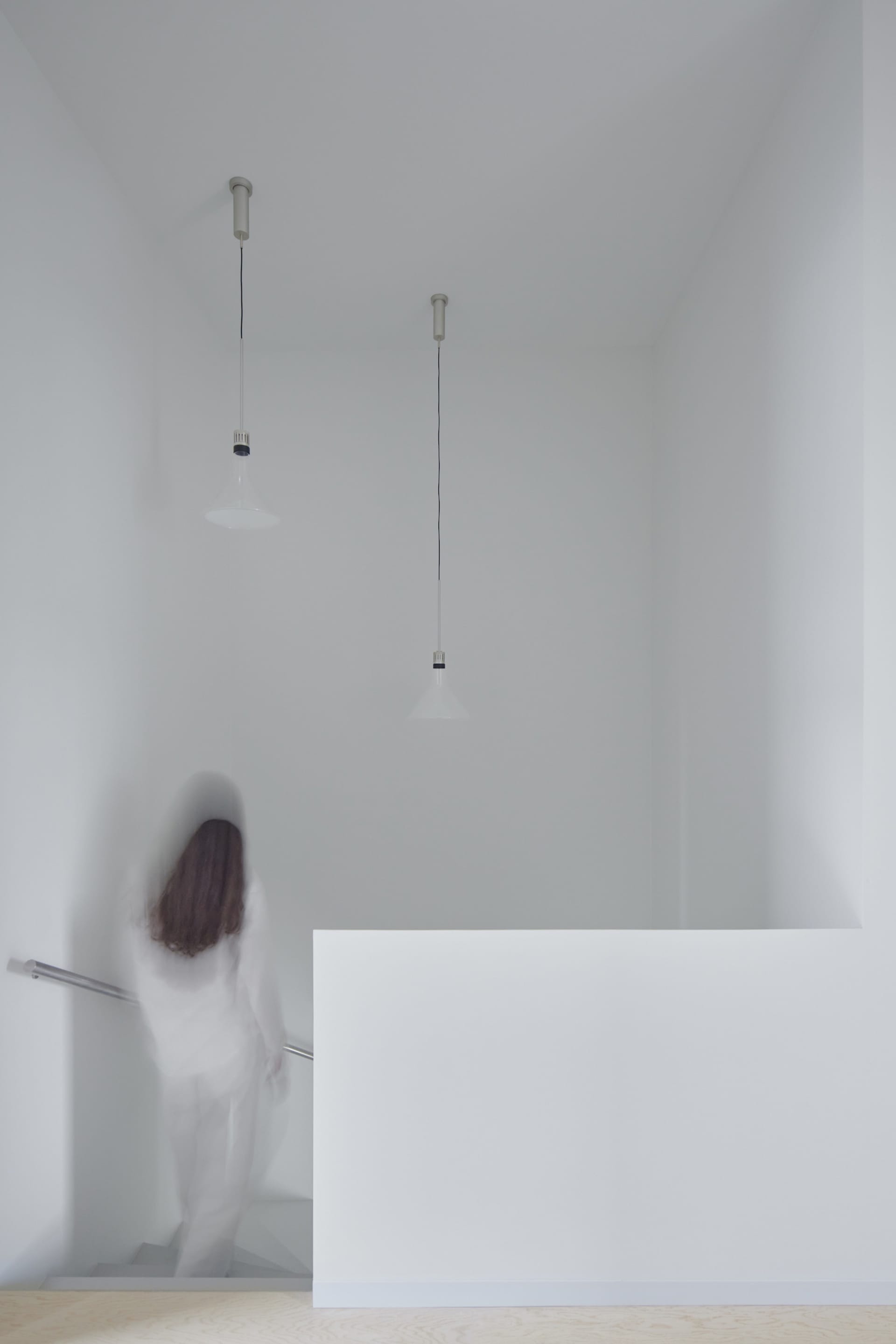 A minimalist white interior space with a person climbing stairs.