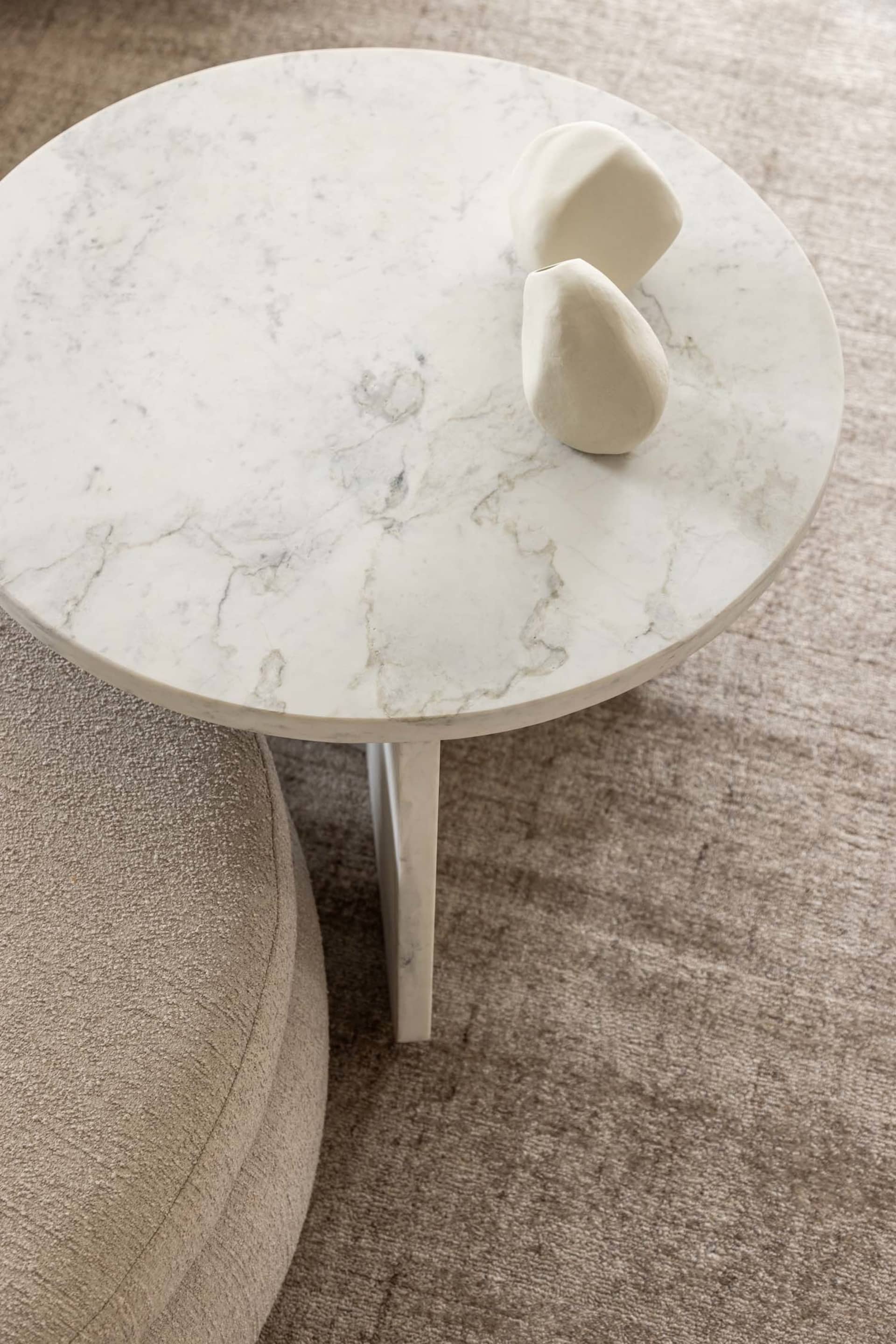 A modern coffee table with a round white marble top adorned with a minimalist white sculpture.
