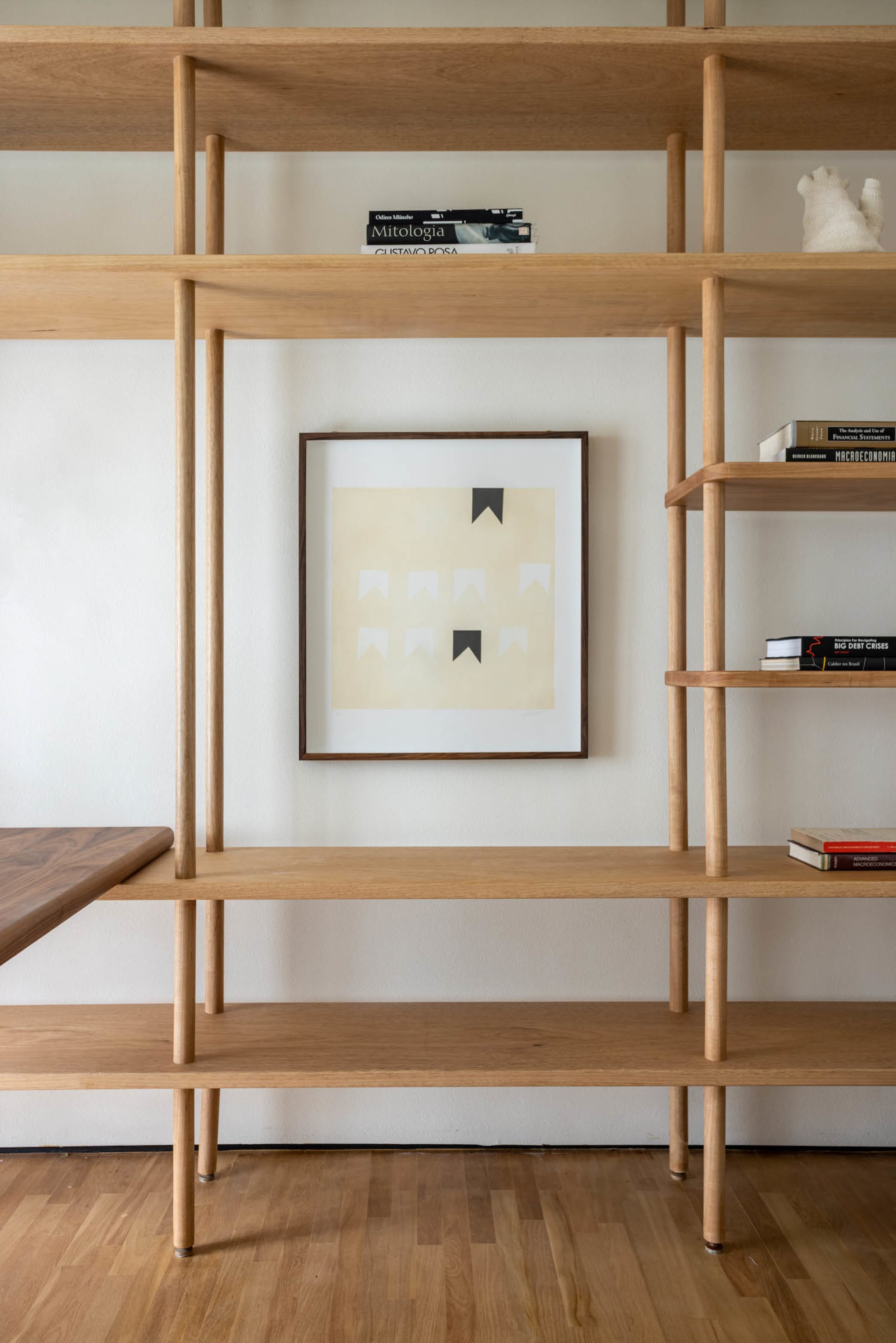 A modern minimalist shelving unit made of wood with a framed abstract art print featuring a black and white design.