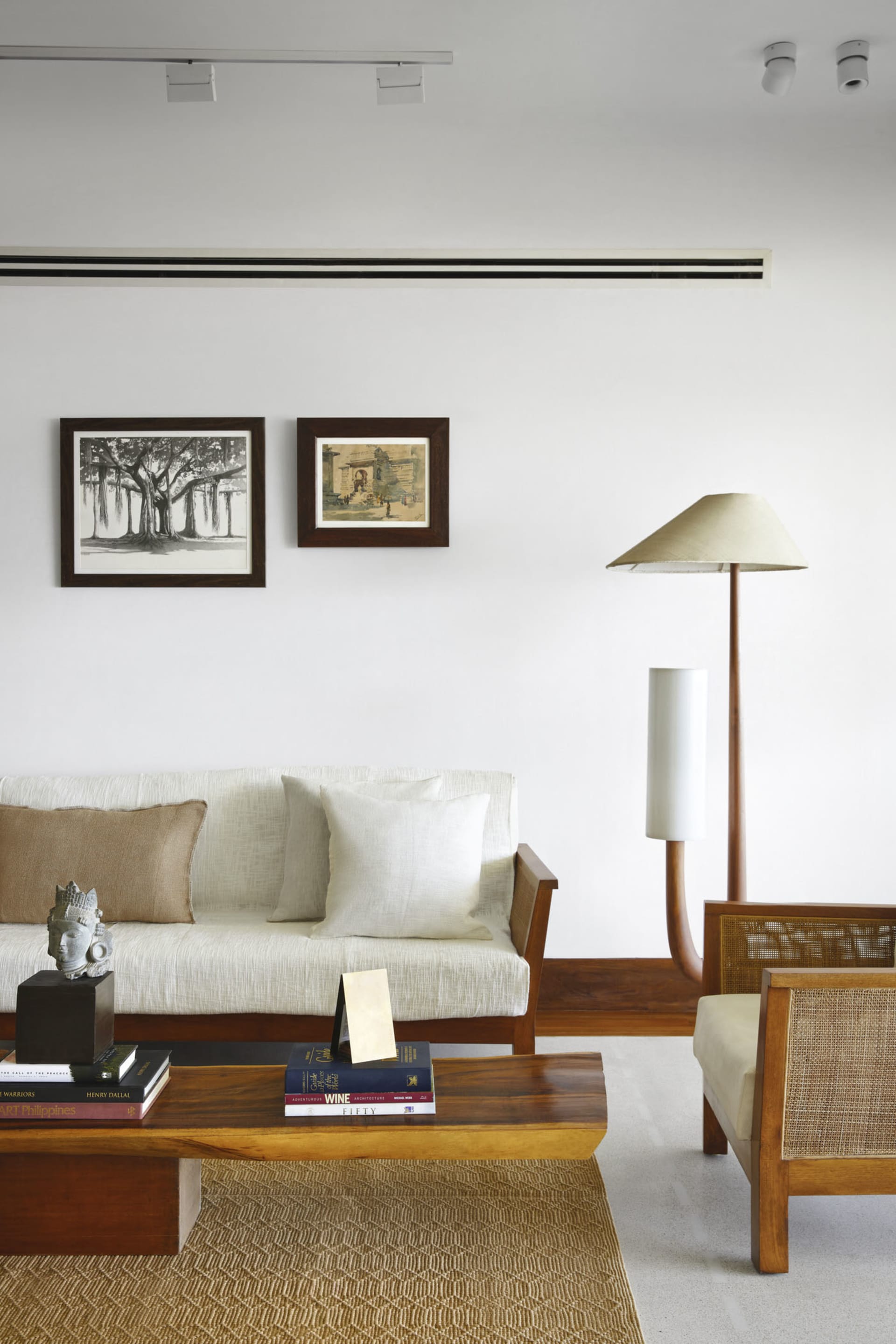 A minimalist living room featuring a wooden sofa, fabric cushions, and a glass coffee table.
