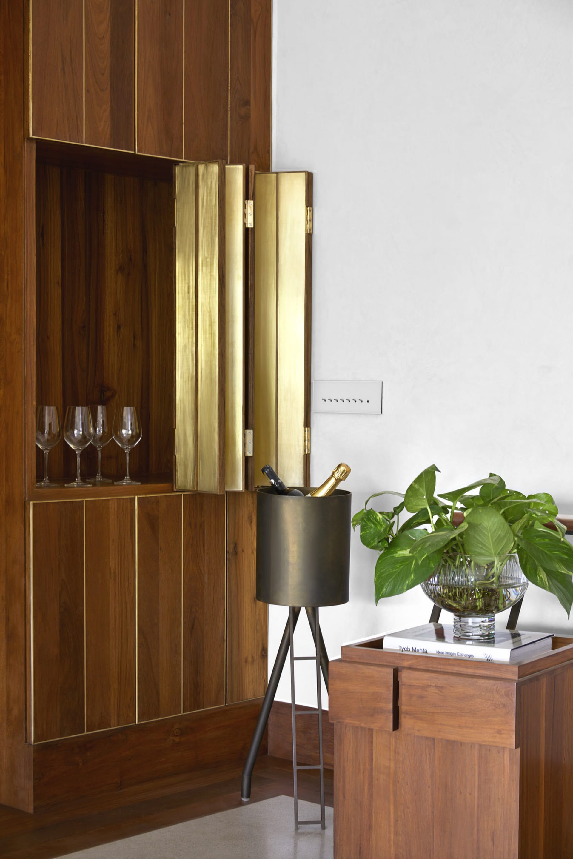 Modern interior space featuring wooden panels with metallic accents, wine glasses, a champagne bucket, and green plant.