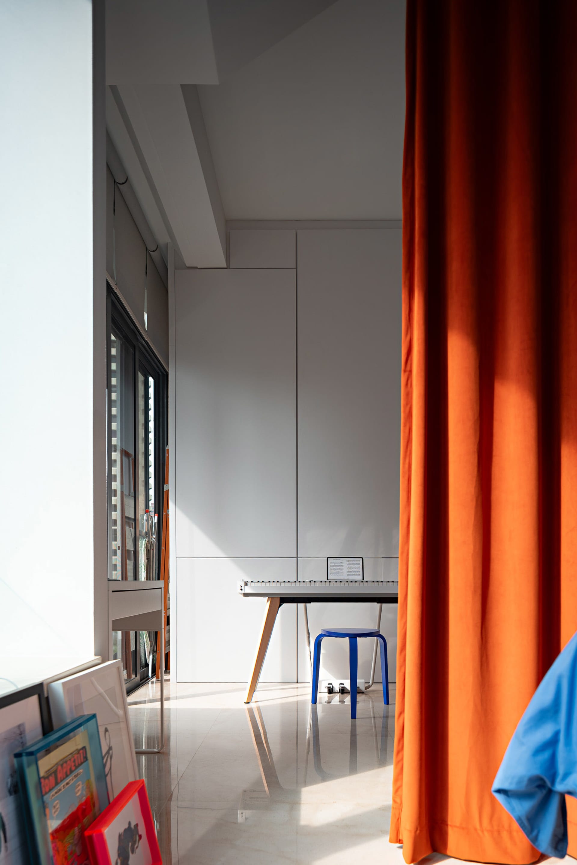 A minimalist office space featuring a sleek, contemporary desk and vibrant orange curtains by the window.