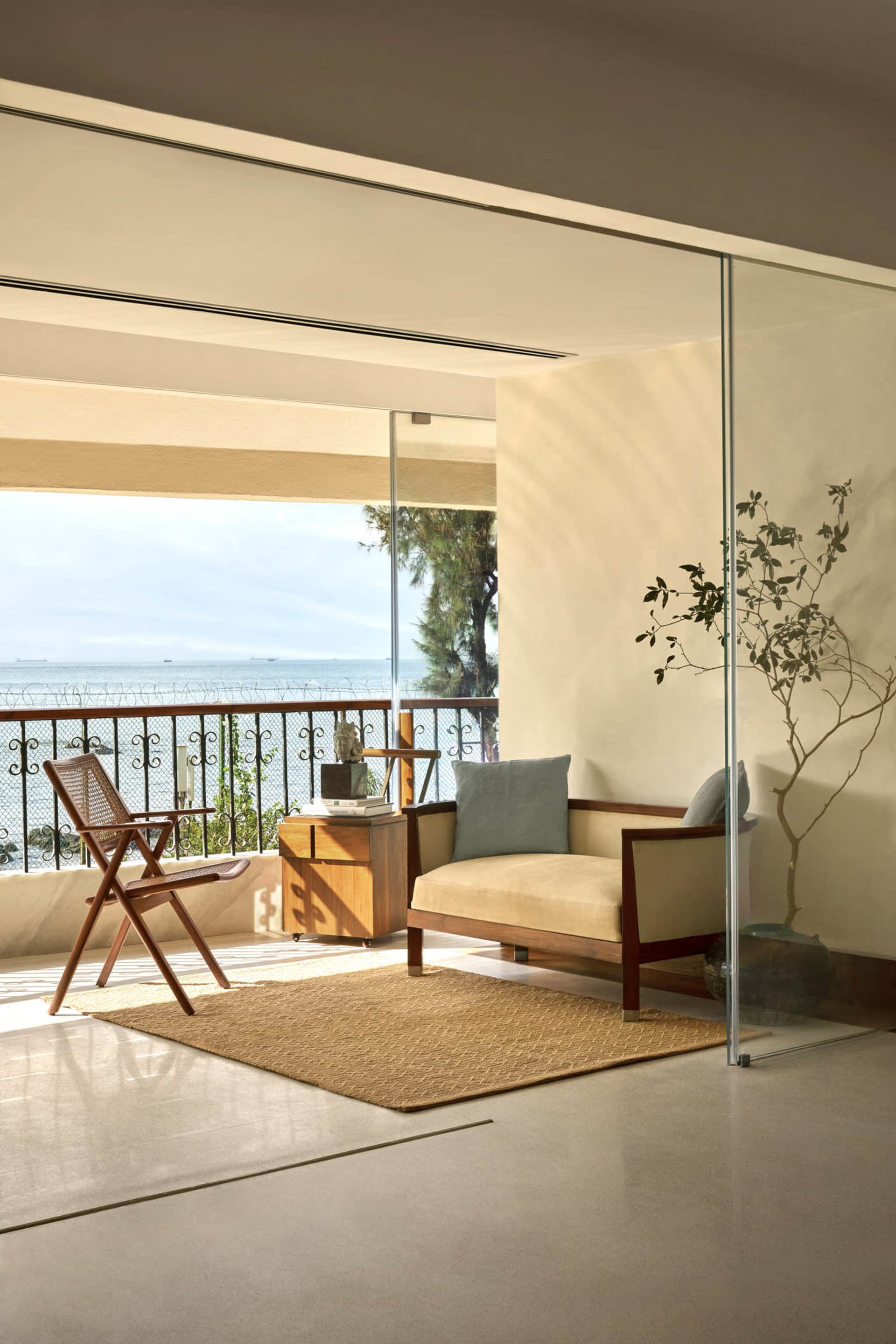 A minimalist living room featuring natural wood furniture, a glass partition, and a view of the ocean.