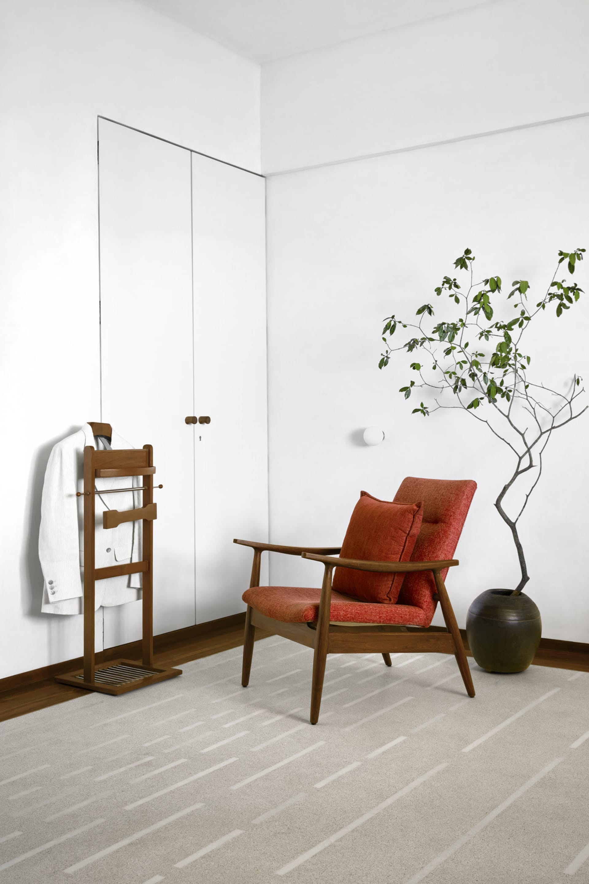 A minimalist living room featuring a wooden armchair with orange cushions and a small potted plant.