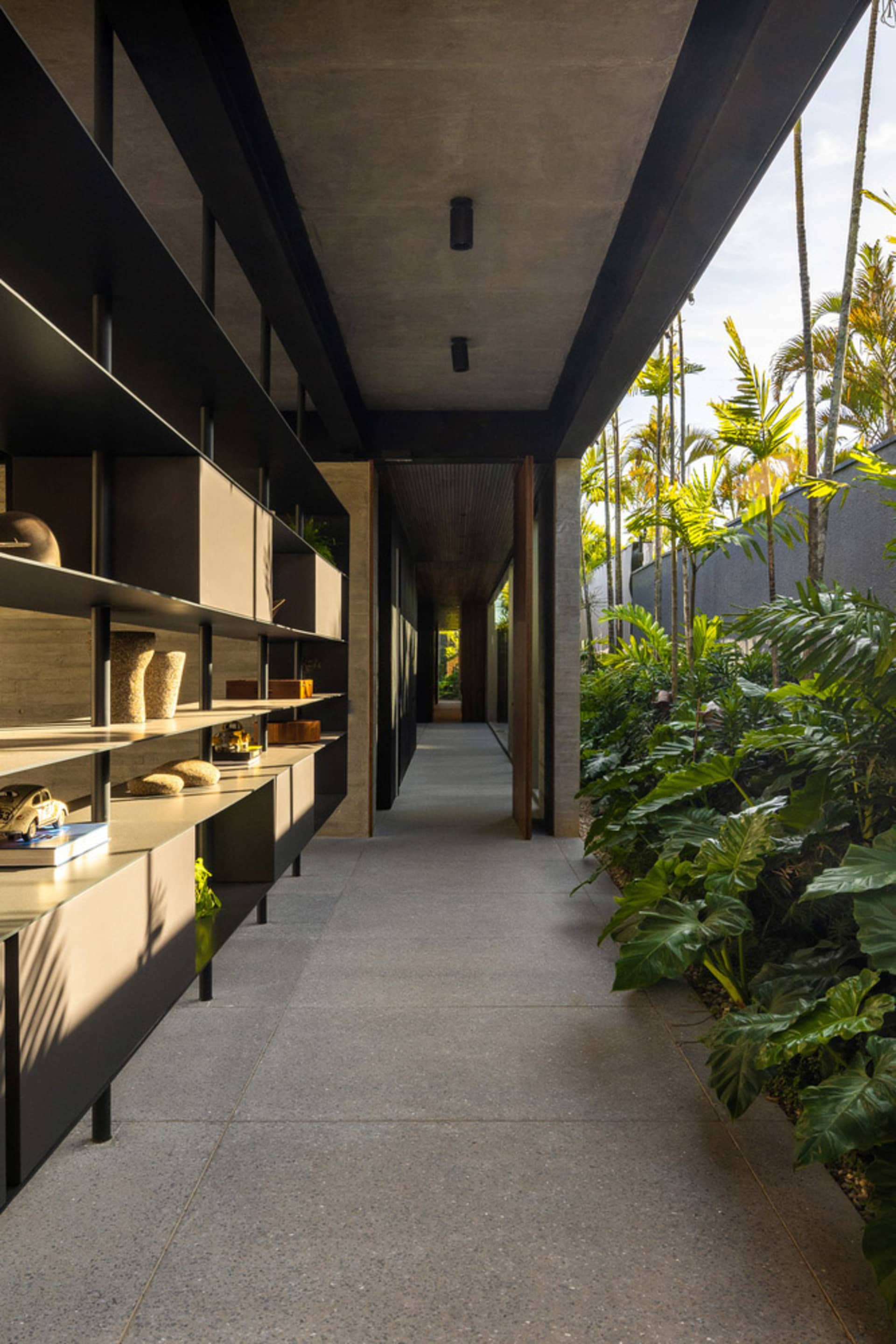 A modern hallway with concrete flooring and walls, featuring built-in shelves and greenery lining the walls.