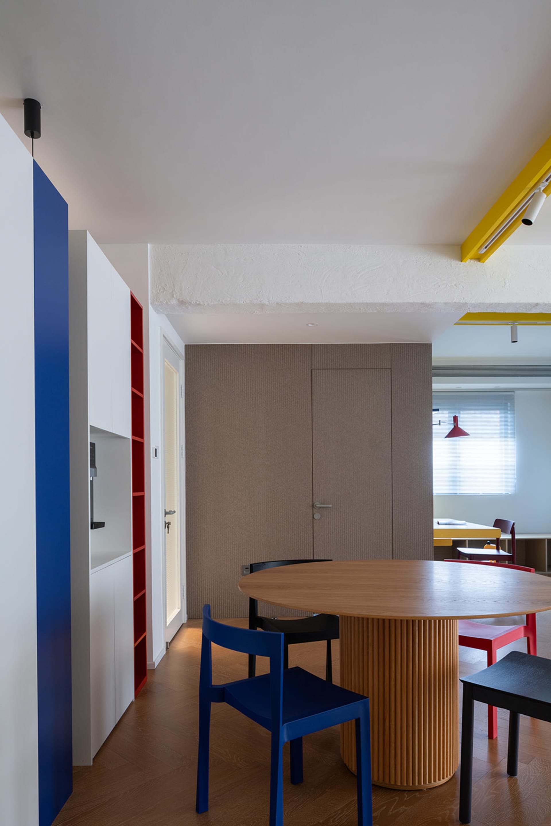 A modern dining area featuring a wooden table surrounded by several chairs in different colors.