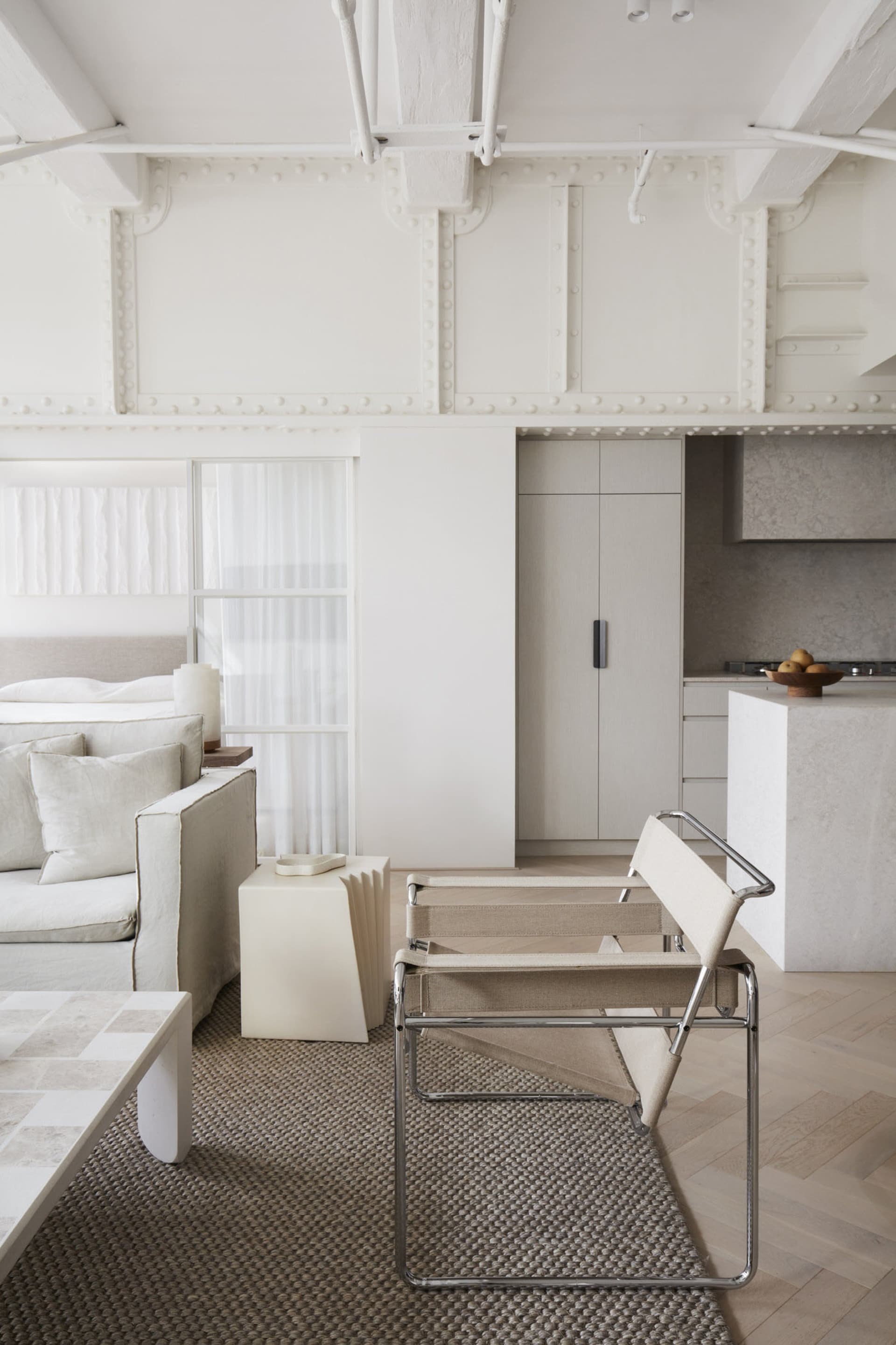 Industrial-style living room with minimalistic design, neutral colors, and exposed ceiling beams.