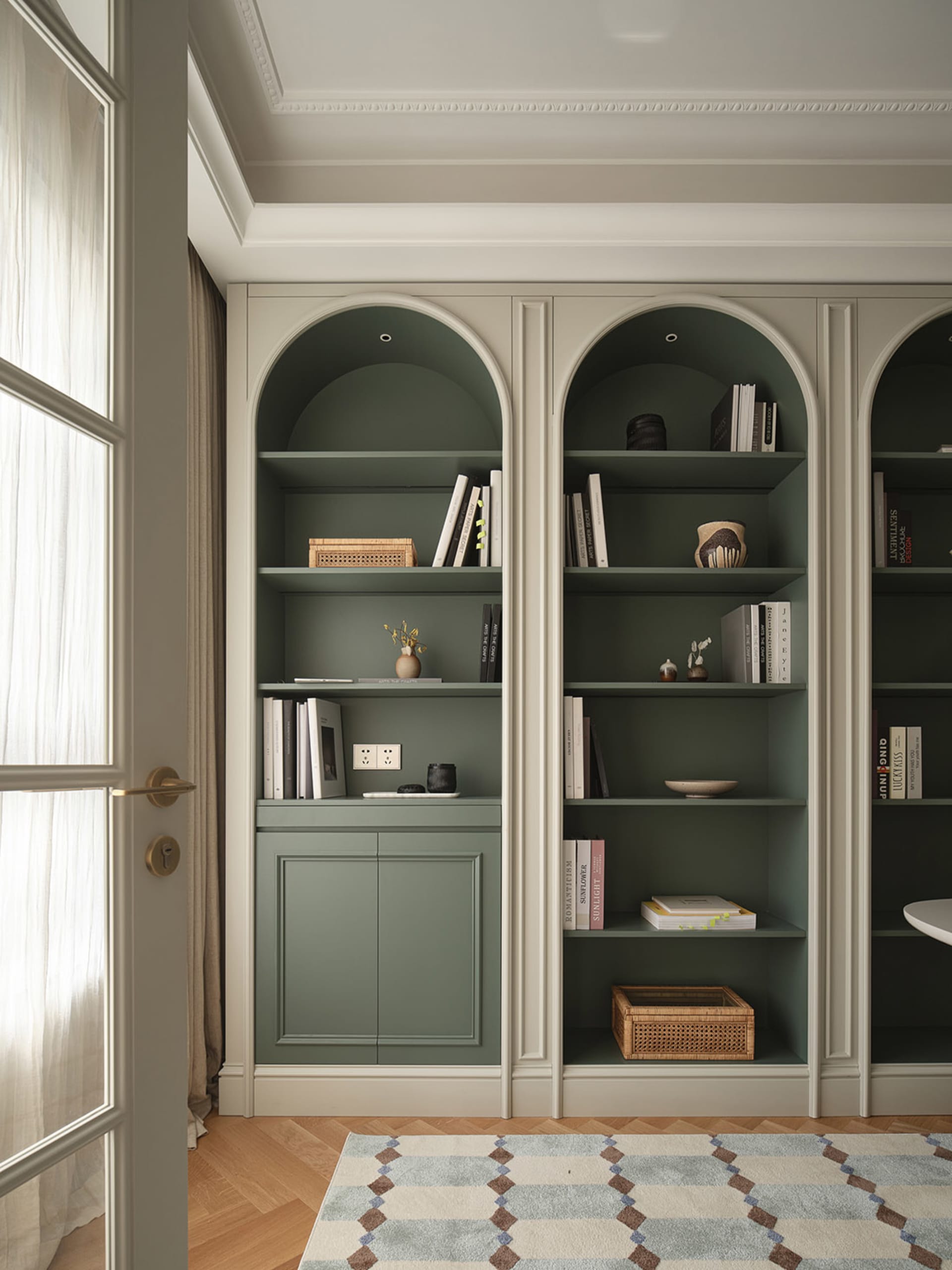 Modern minimalist home library featuring green paneled walls and wooden cabinetry, with books and decorative items on shelves