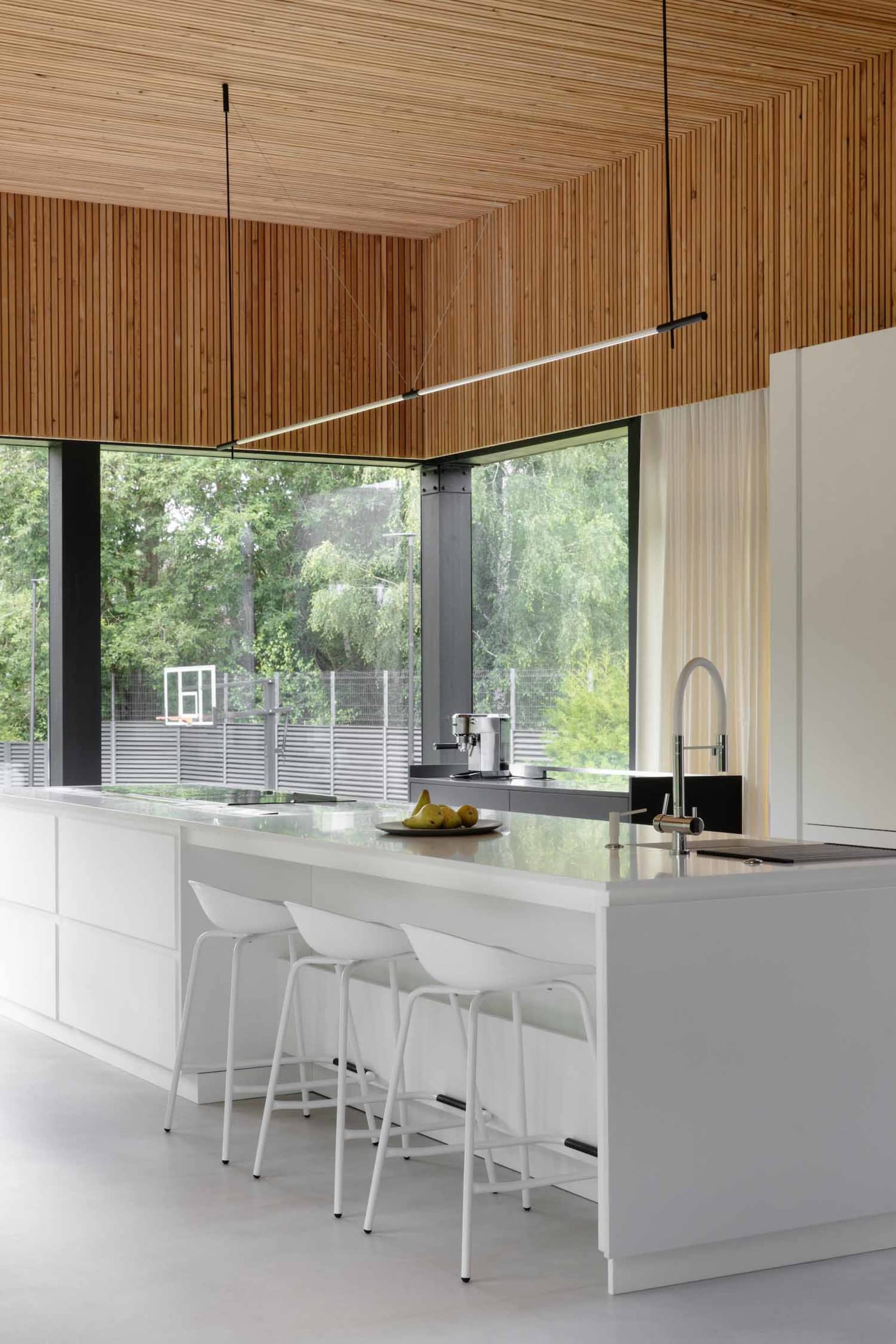 Modern kitchen with white cabinets, wooden walls, and a large window overlooking greenery.