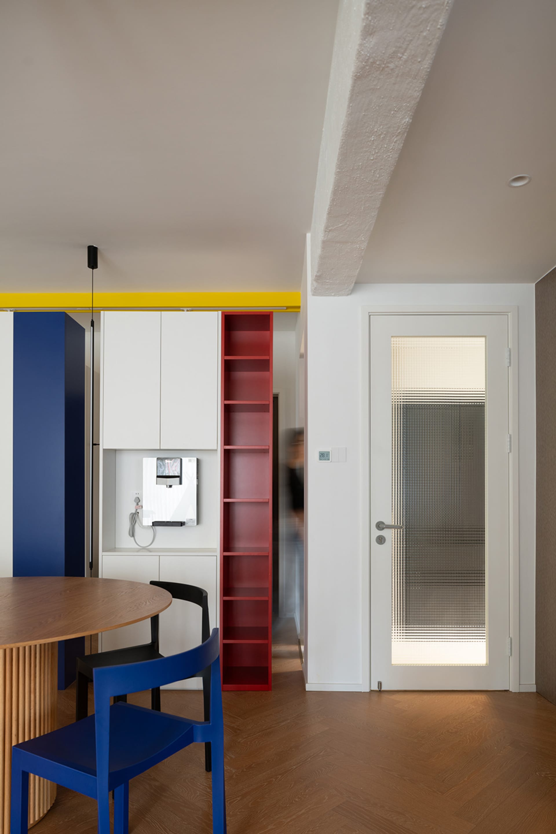 Modern apartment interior with red bookshelf and wooden table and chairs.