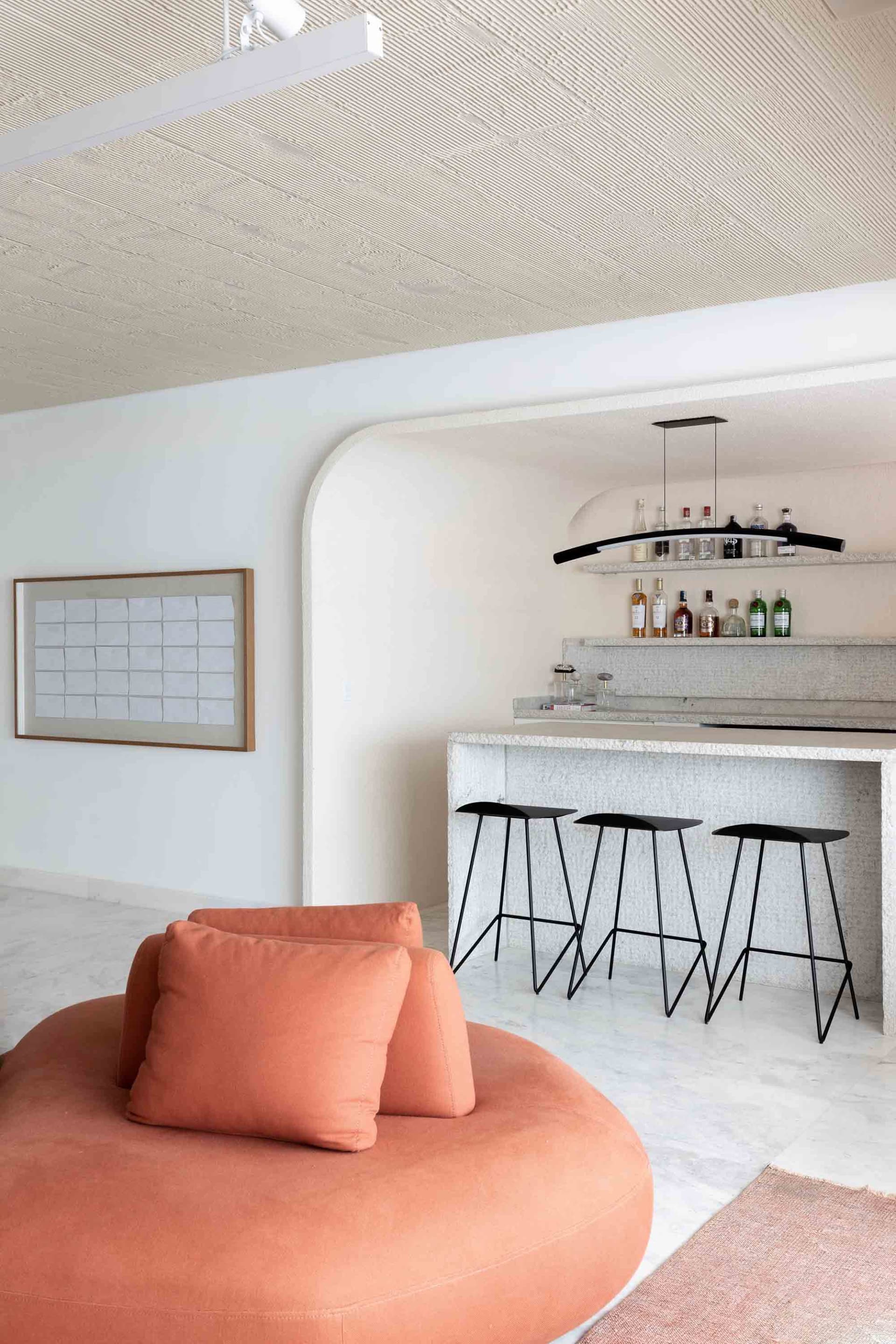Spacious modern living room with large circular peach-colored lounge chair and concrete bar area with shelves and black stool