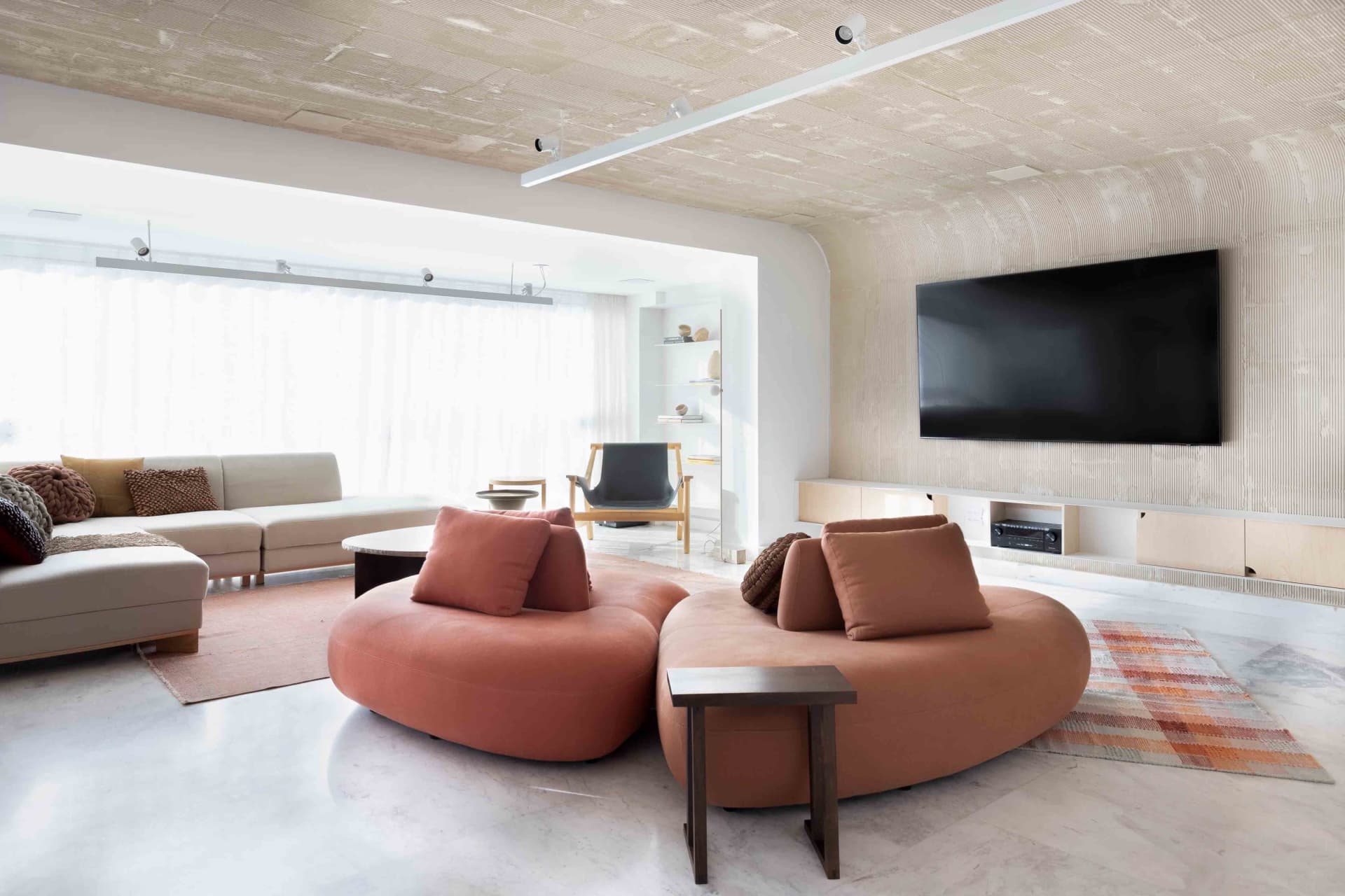 A modern living room featuring a circular sofa with textured upholstery, white walls with vertical detailing, and a large win