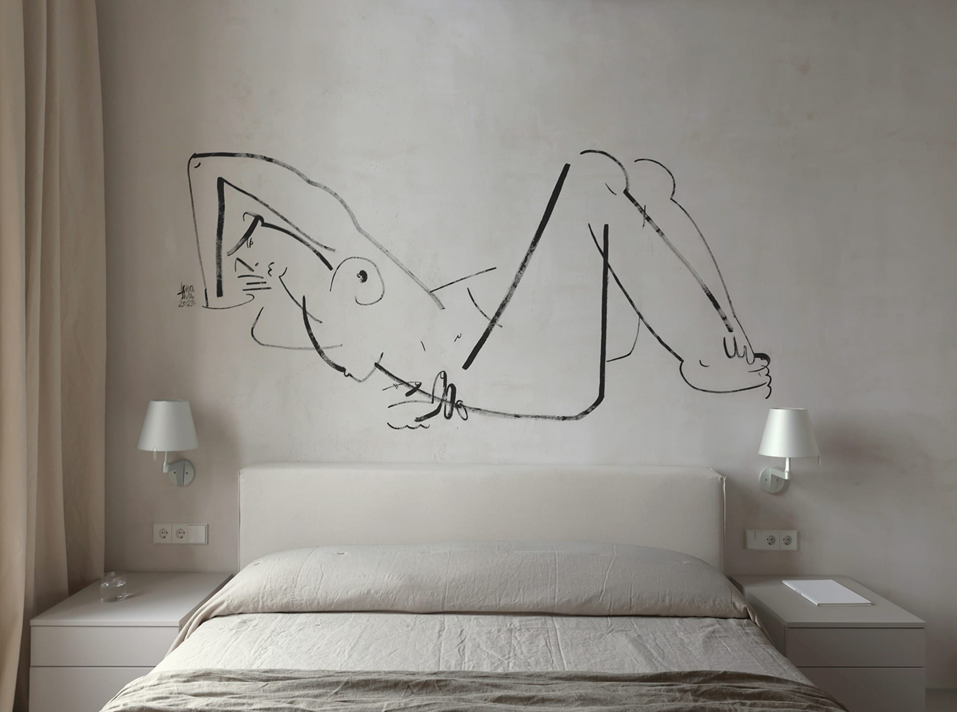A minimalist bedroom featuring a bed with a white headboard and linens, a wall drawing of a reclining figure, and bedside lam