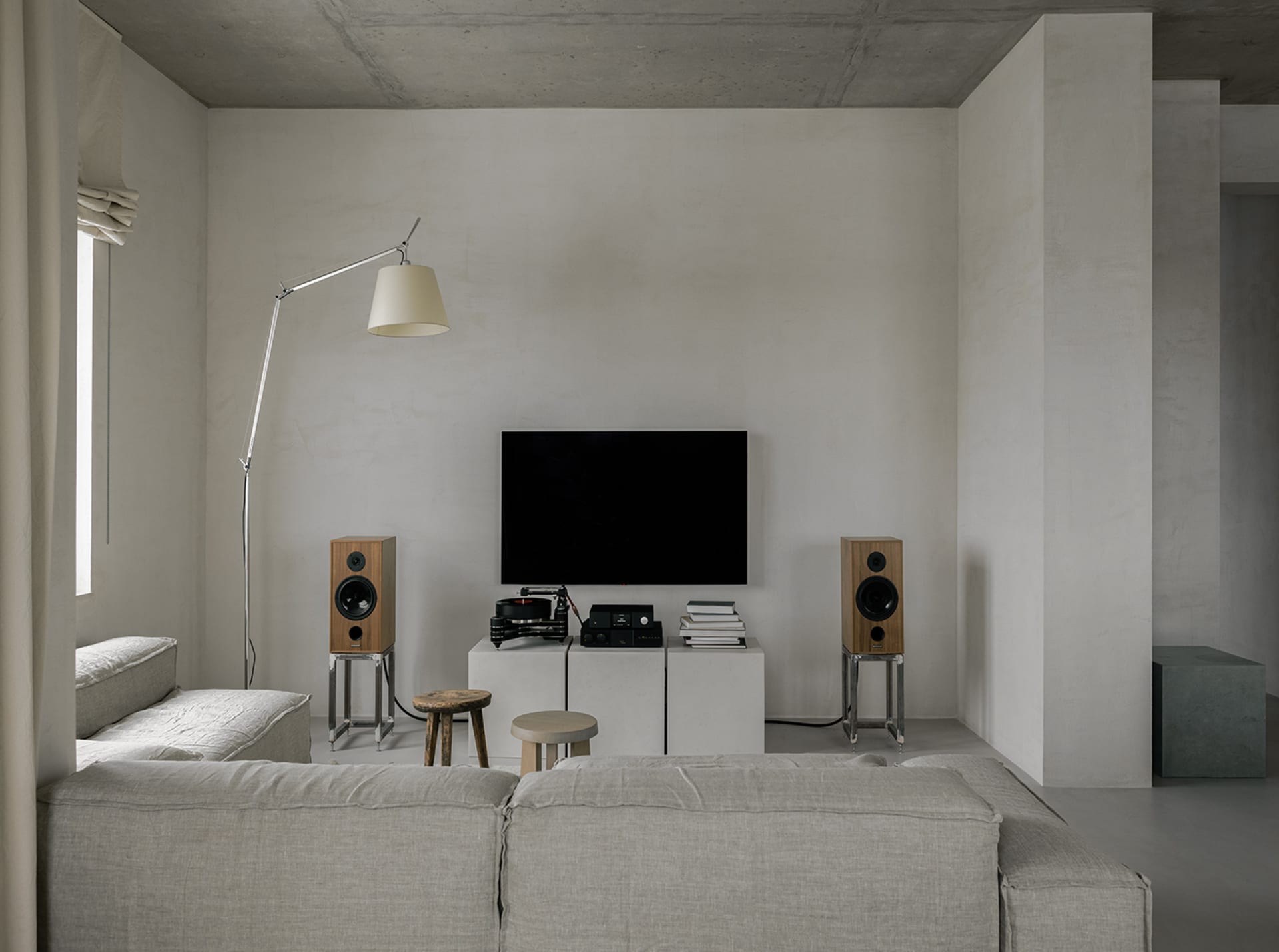 A minimalist living room with concrete walls, a large sofa, and floor-to-ceiling windows.