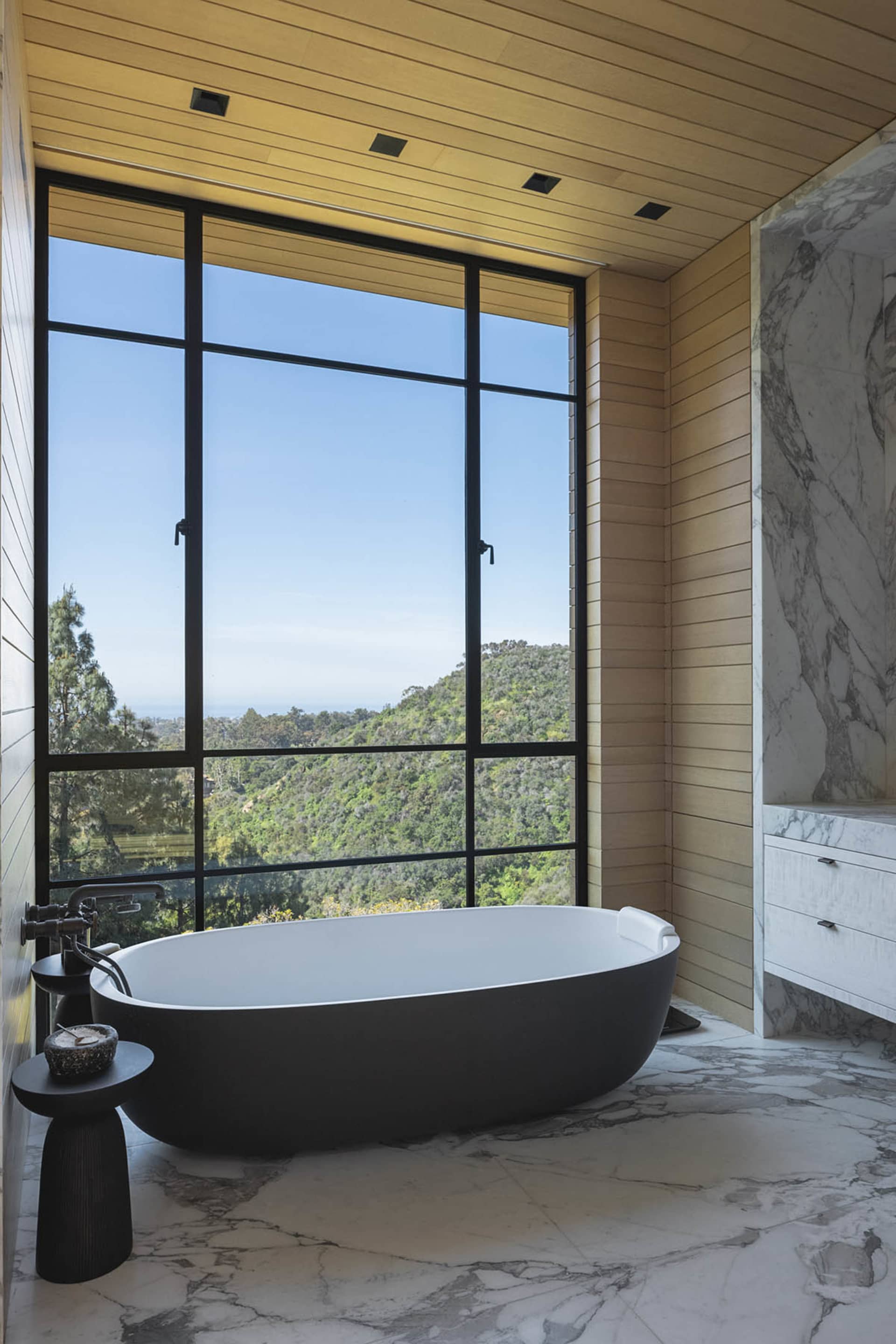 Modern bathroom featuring a freestanding bathtub with a view of the mountains, surrounded by marble and concrete materials.