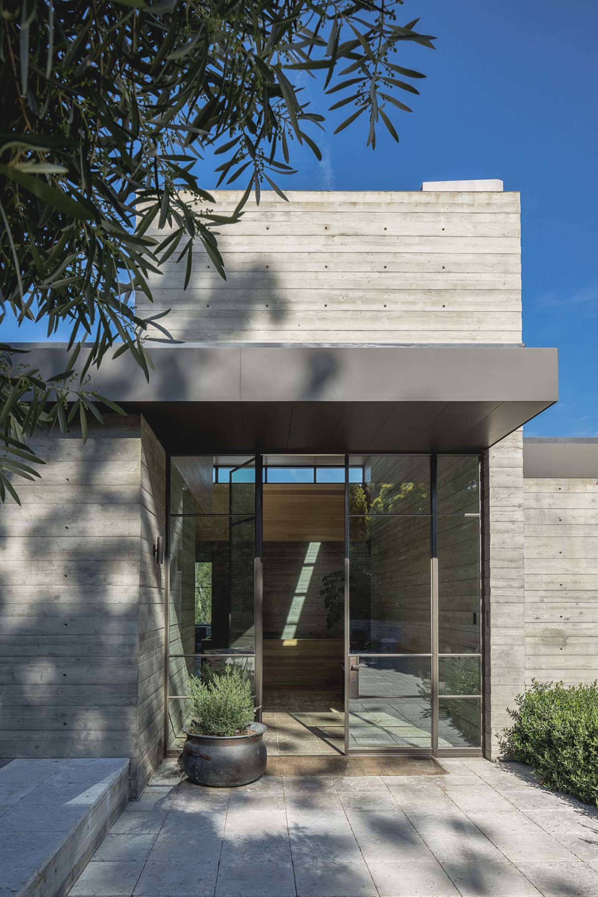 A modern residential entryway featuring a concrete wall and large glass doors.