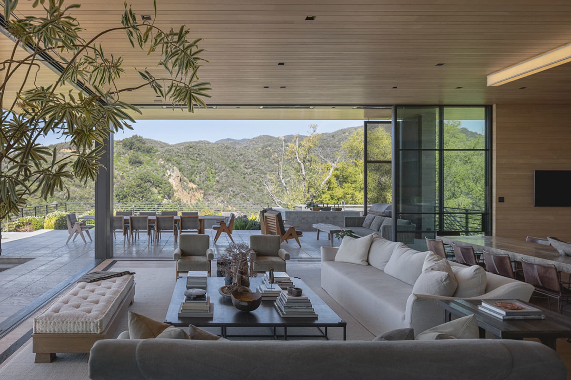 A modern living room featuring wood, glass, fabric, and concrete materials, with comfortable seating and a large window overl