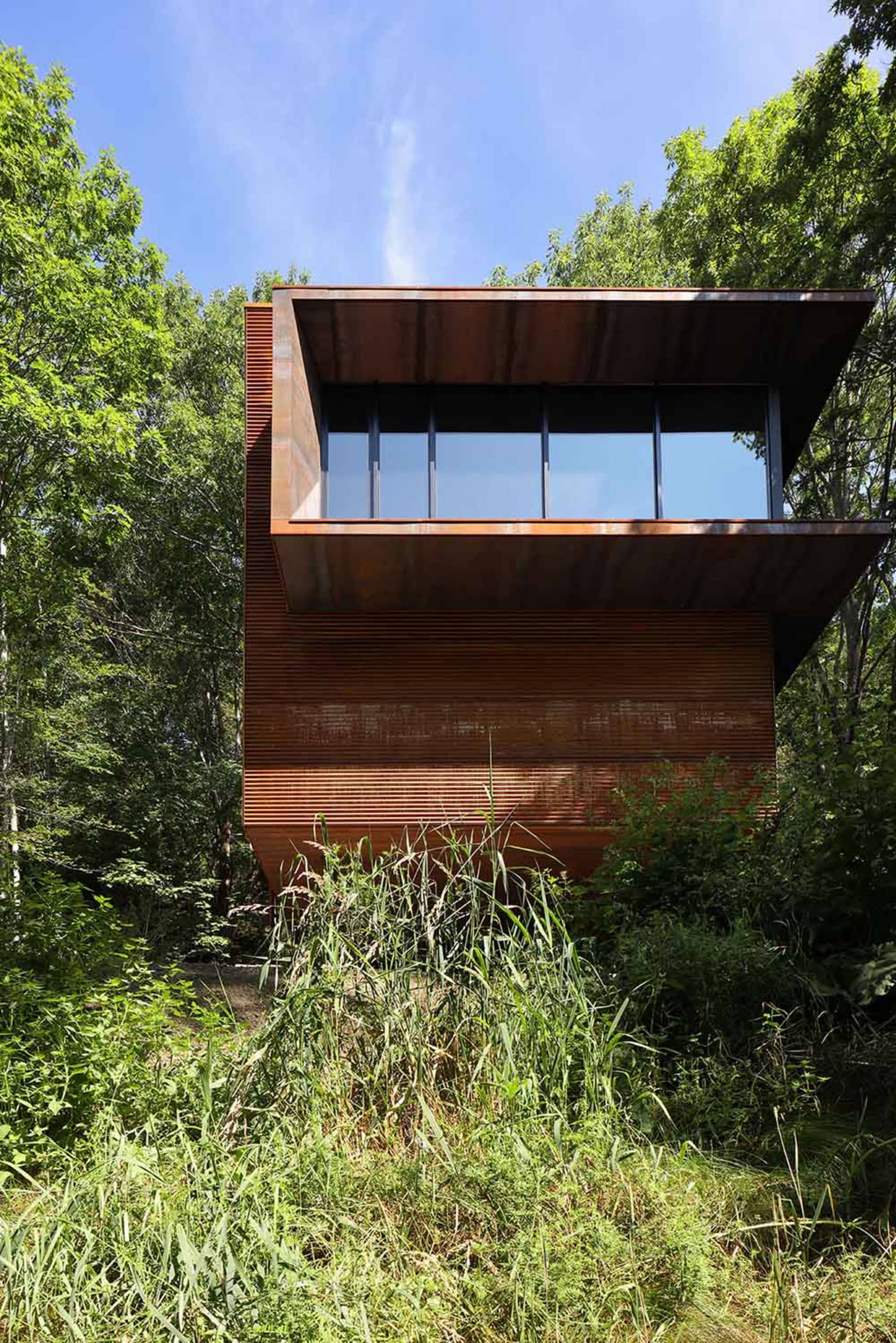 Modern residential house with steel exterior and large windows in a forest setting.