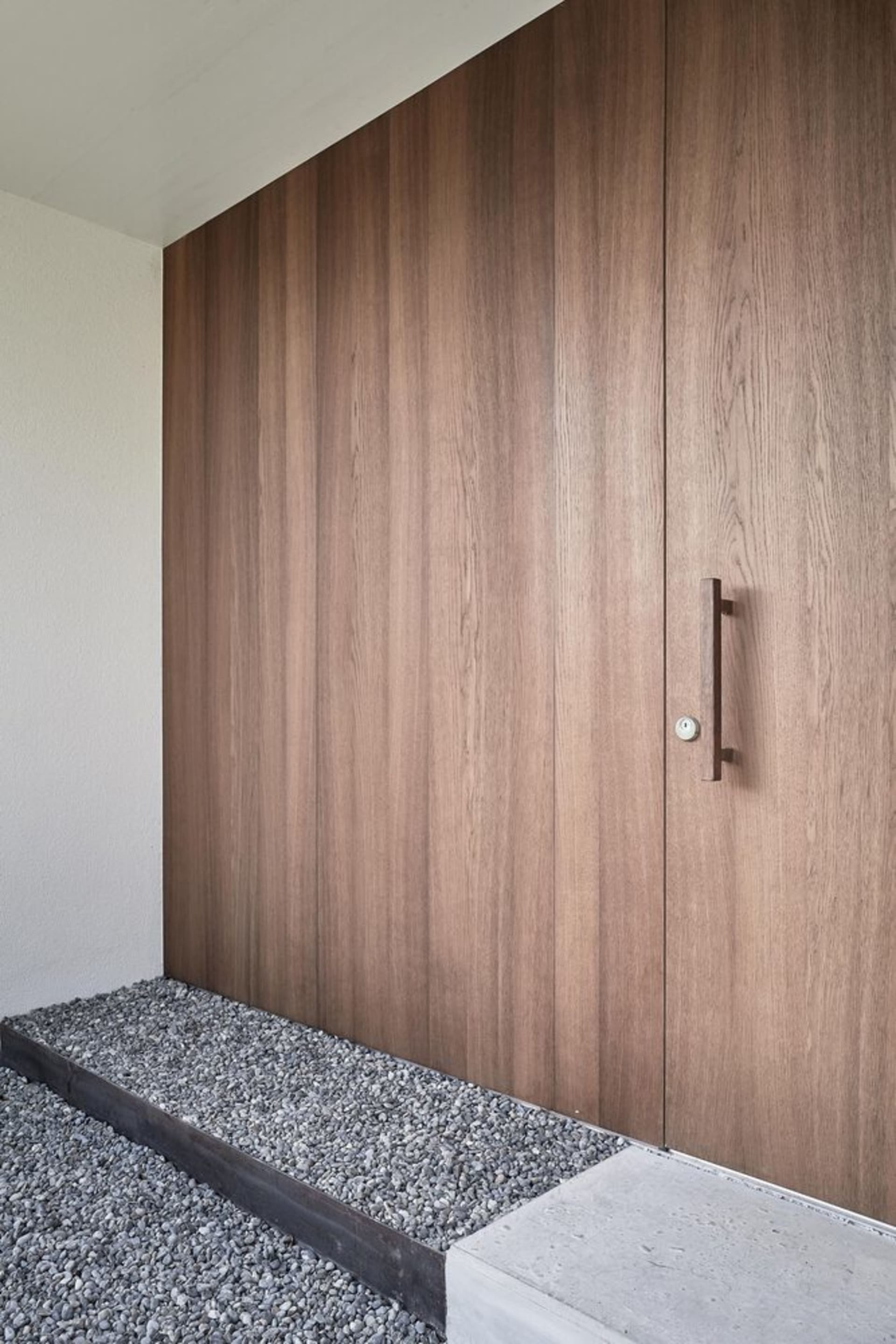 A modern front entry featuring a wooden door and gravel pathway.