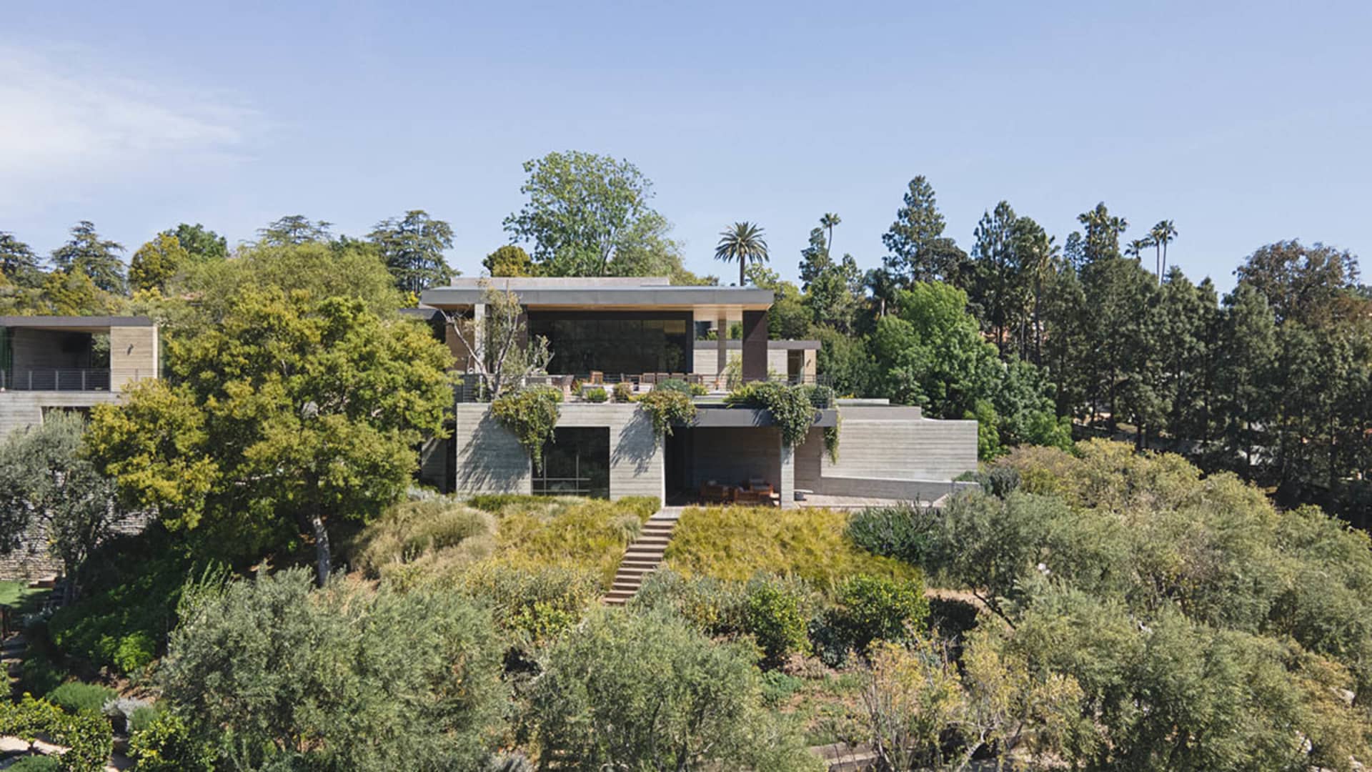 A modern residence with a concrete exterior surrounded by lush greenery and trees.