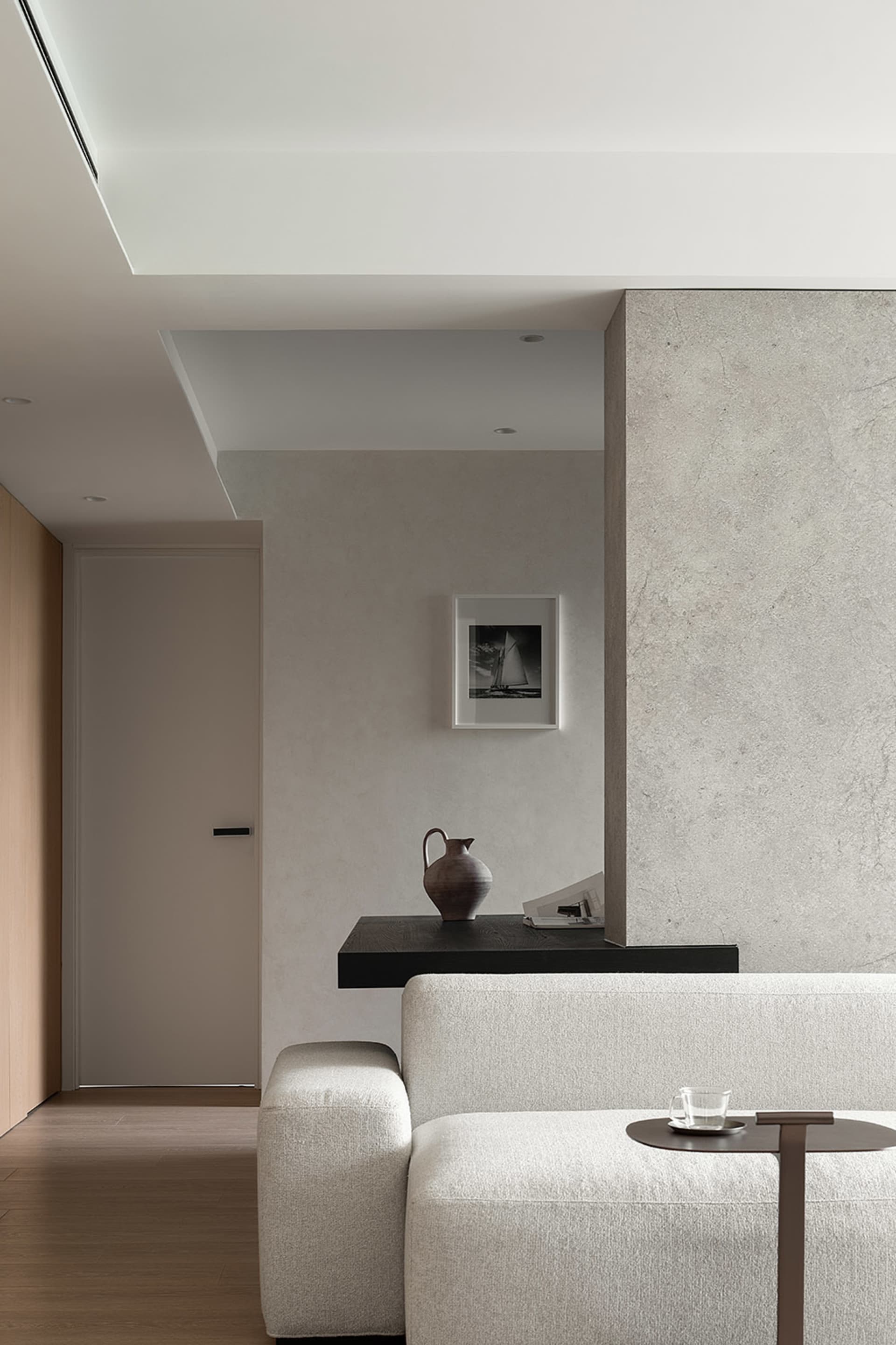 A minimalist living room with concrete walls, a white sofa, and a coffee table with a glass cup.
