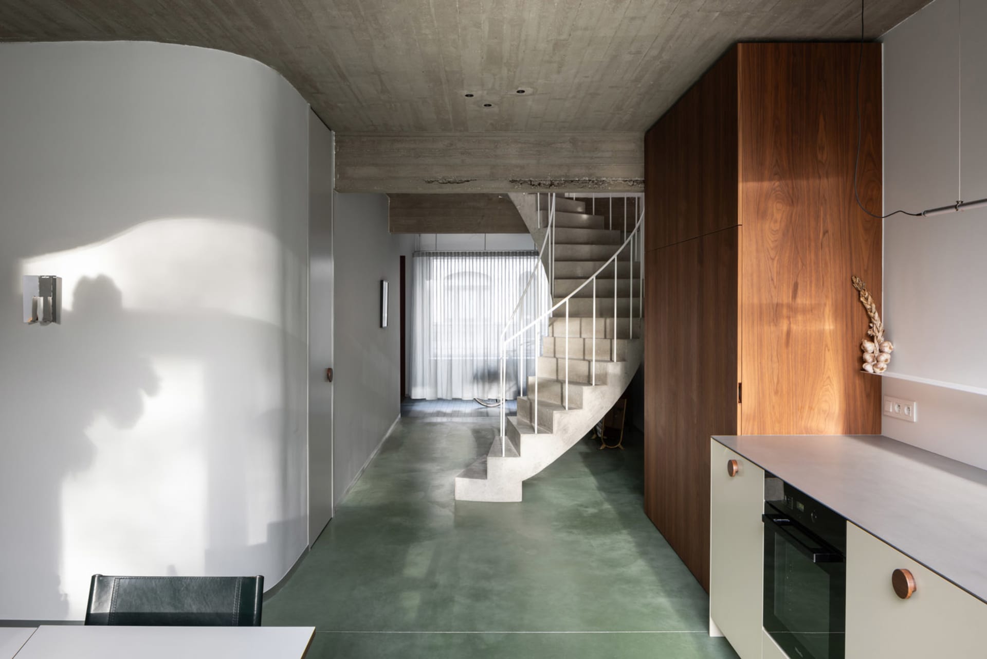 A modern kitchen with a concrete floor and a staircase leading to another level.