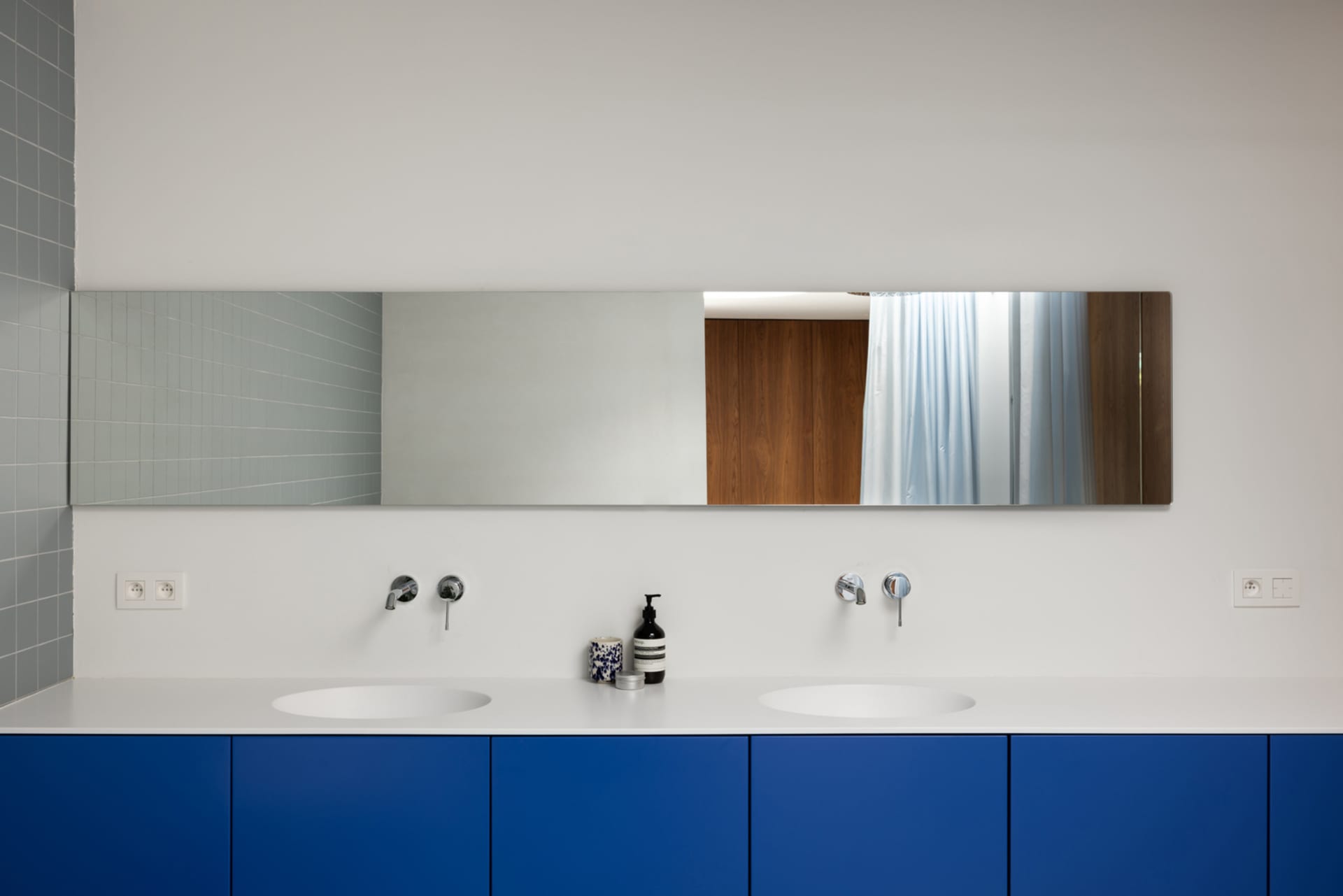 Minimalist bathroom with blue cabinets, metallic faucets, and wood accents.