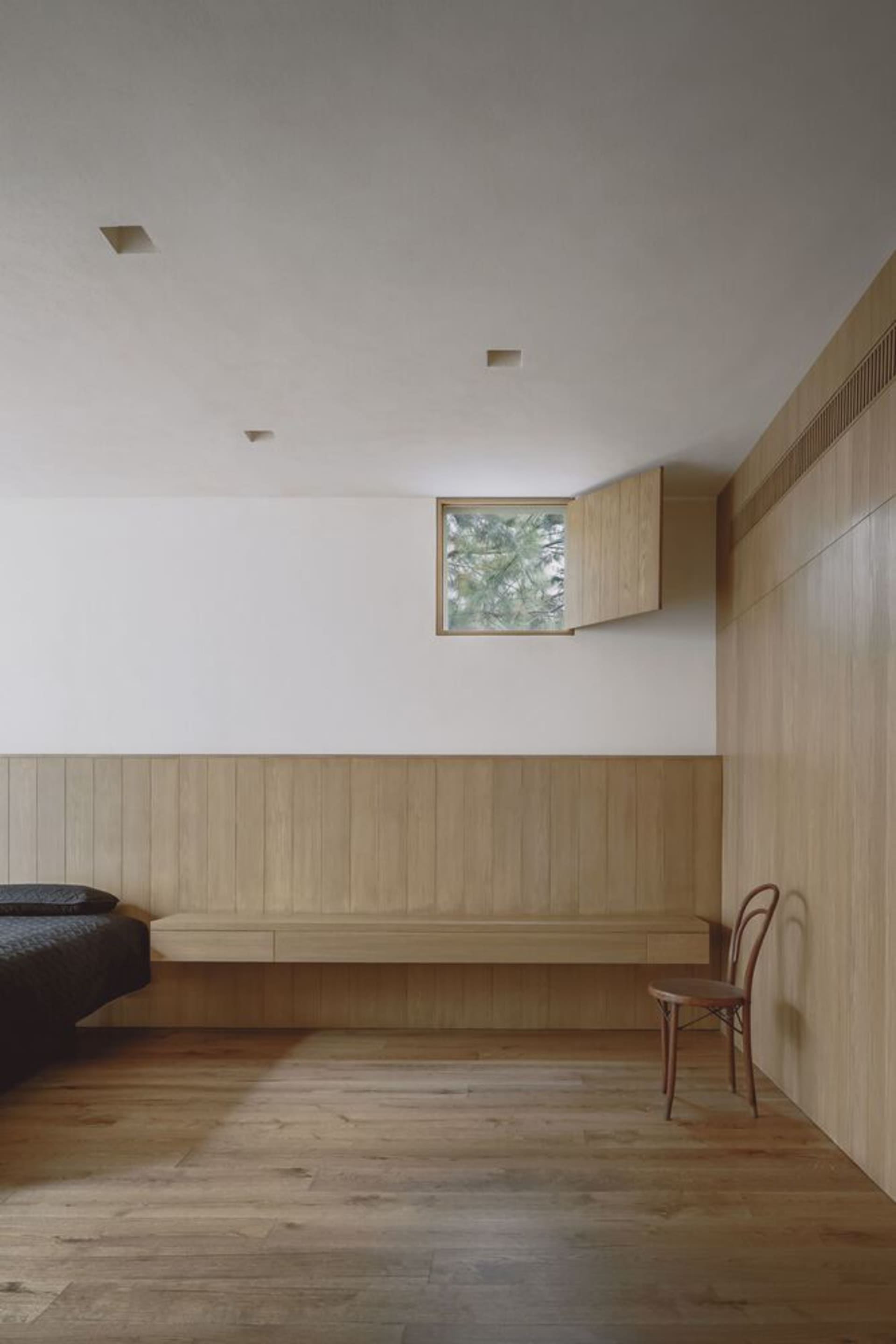 Minimalist bedroom featuring light-colored wooden paneling and a small window
