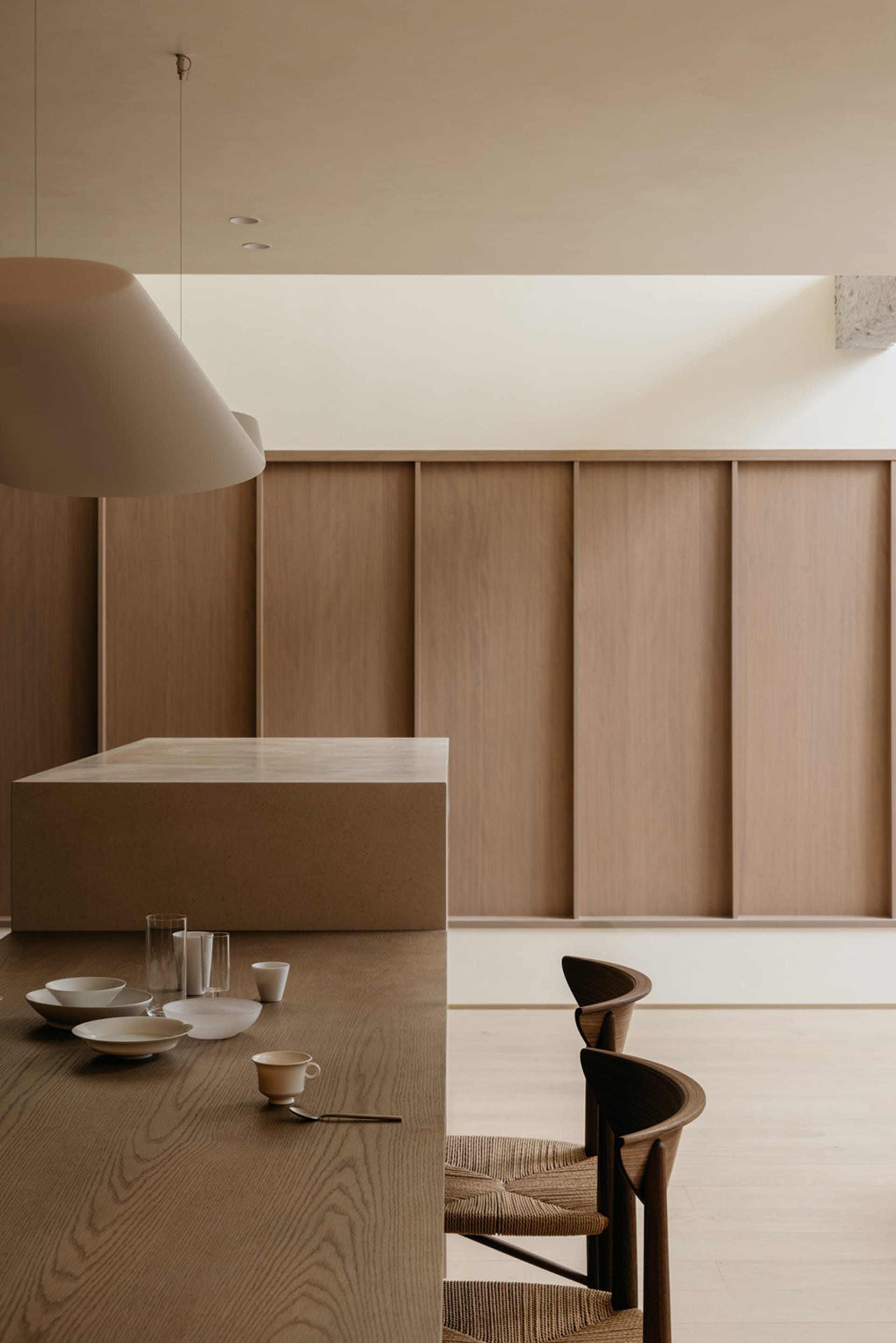 A minimalist kitchen with wooden finishes, a stone countertop, and a large pendant light.