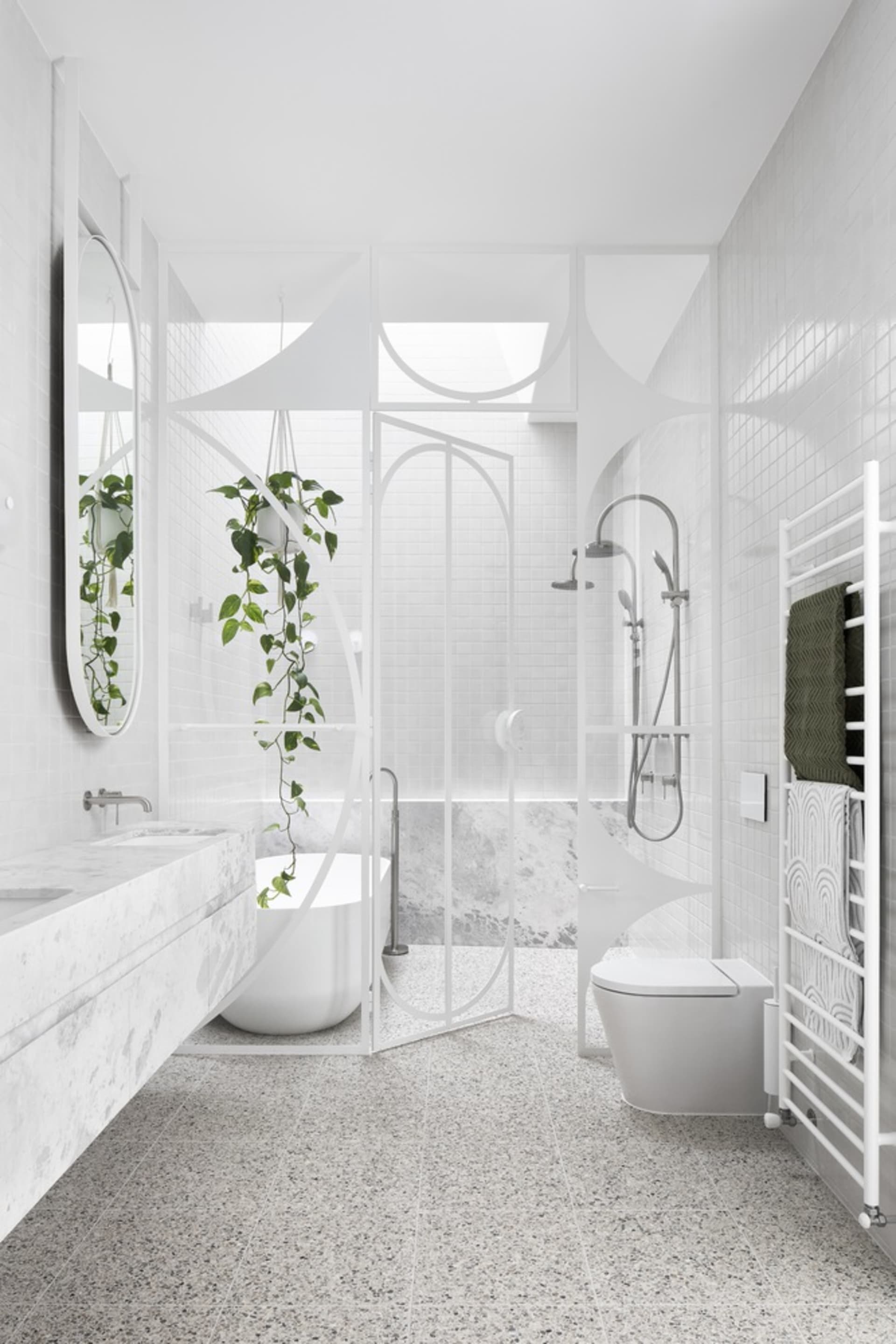 A modern bathroom featuring white terrazzo flooring and minimalist white fixtures, with a single potted plant and a large mir
