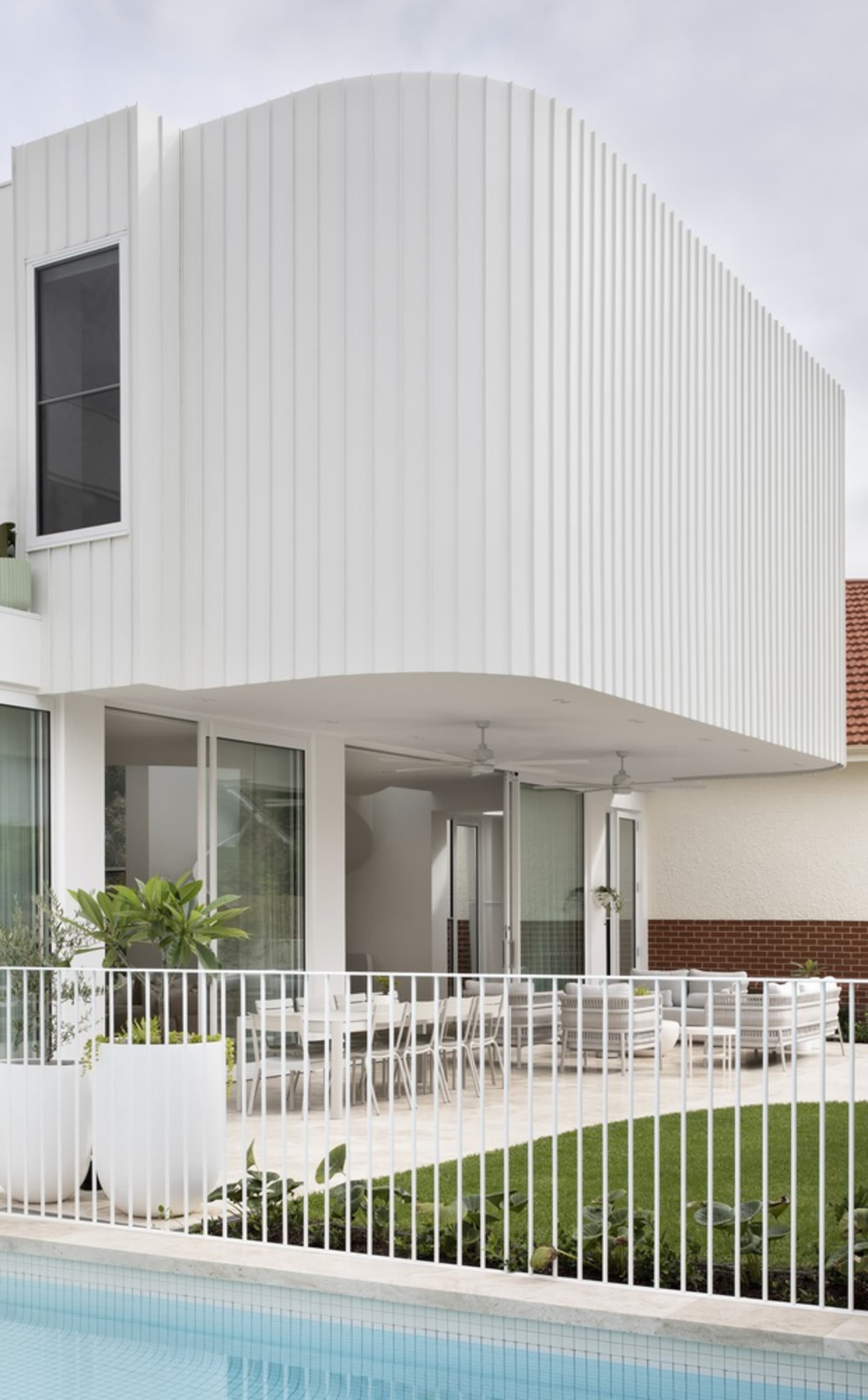 Modern exterior with white concrete poolside lounge area featuring curved structural design and white metal railings.