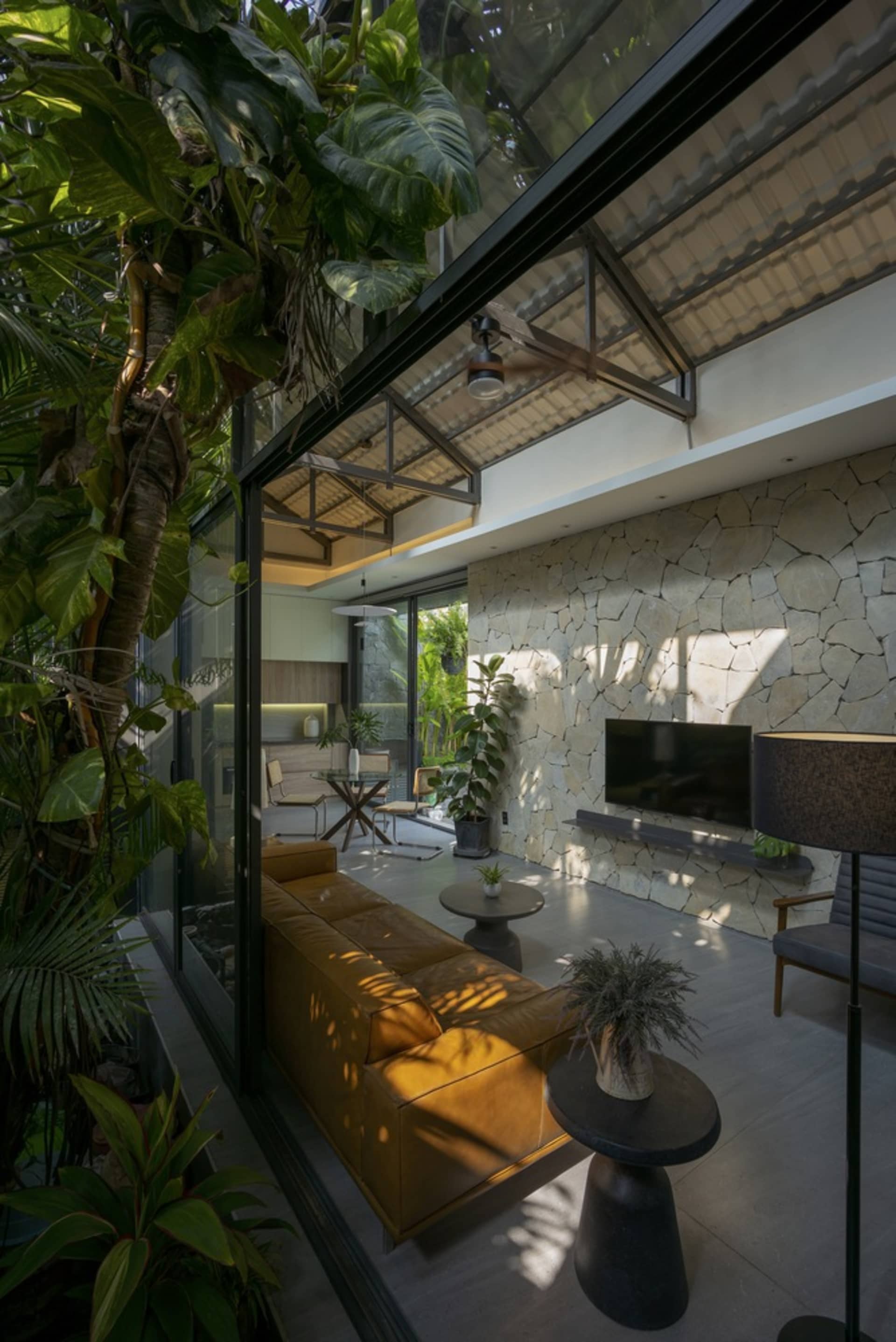 A modern living room featuring glass walls, stone accents, and concrete floors, with a comfortable seating area and a flat-sc