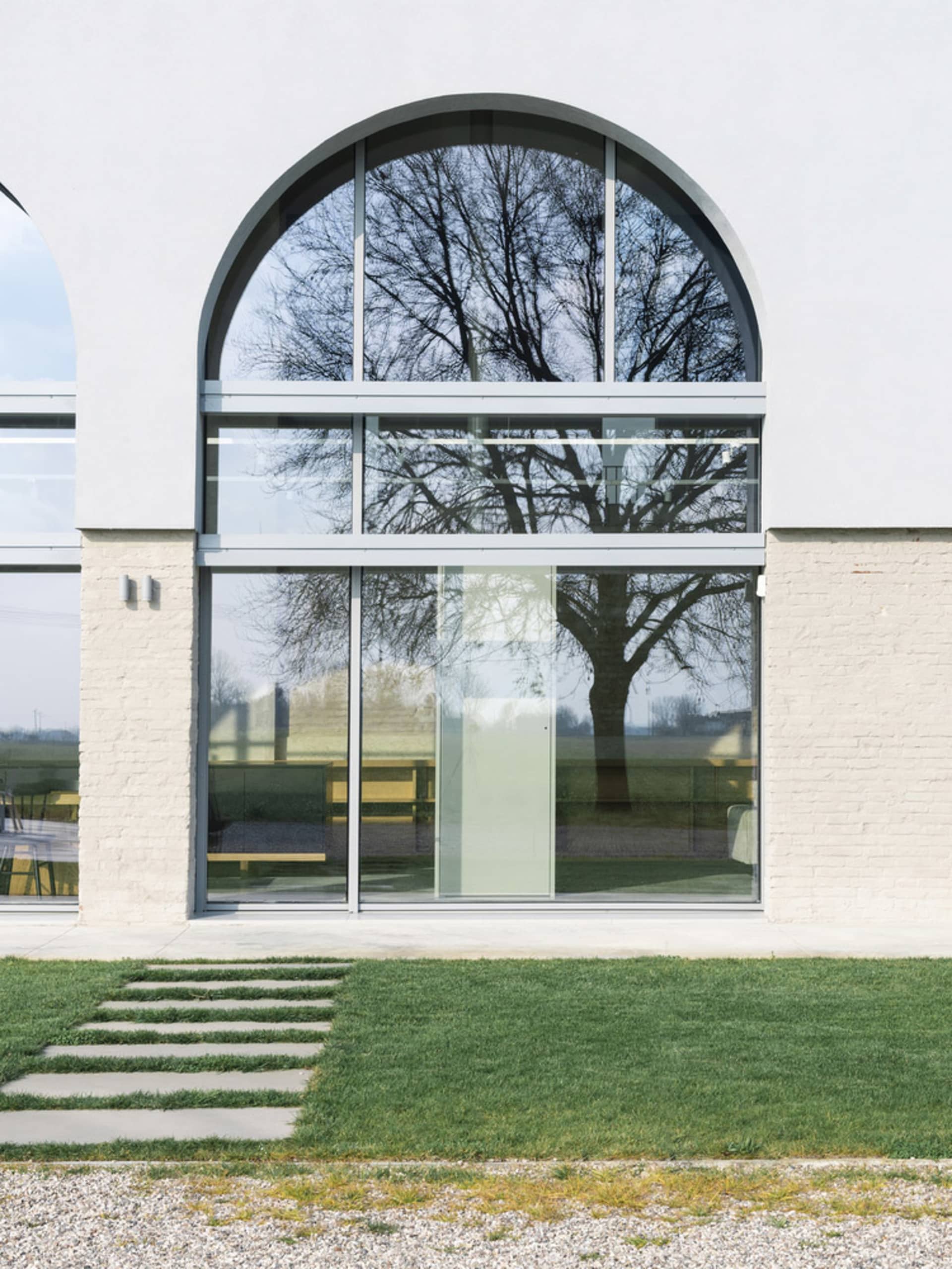 A large, double-height glass window with an arched top in a minimalistic architectural setting.