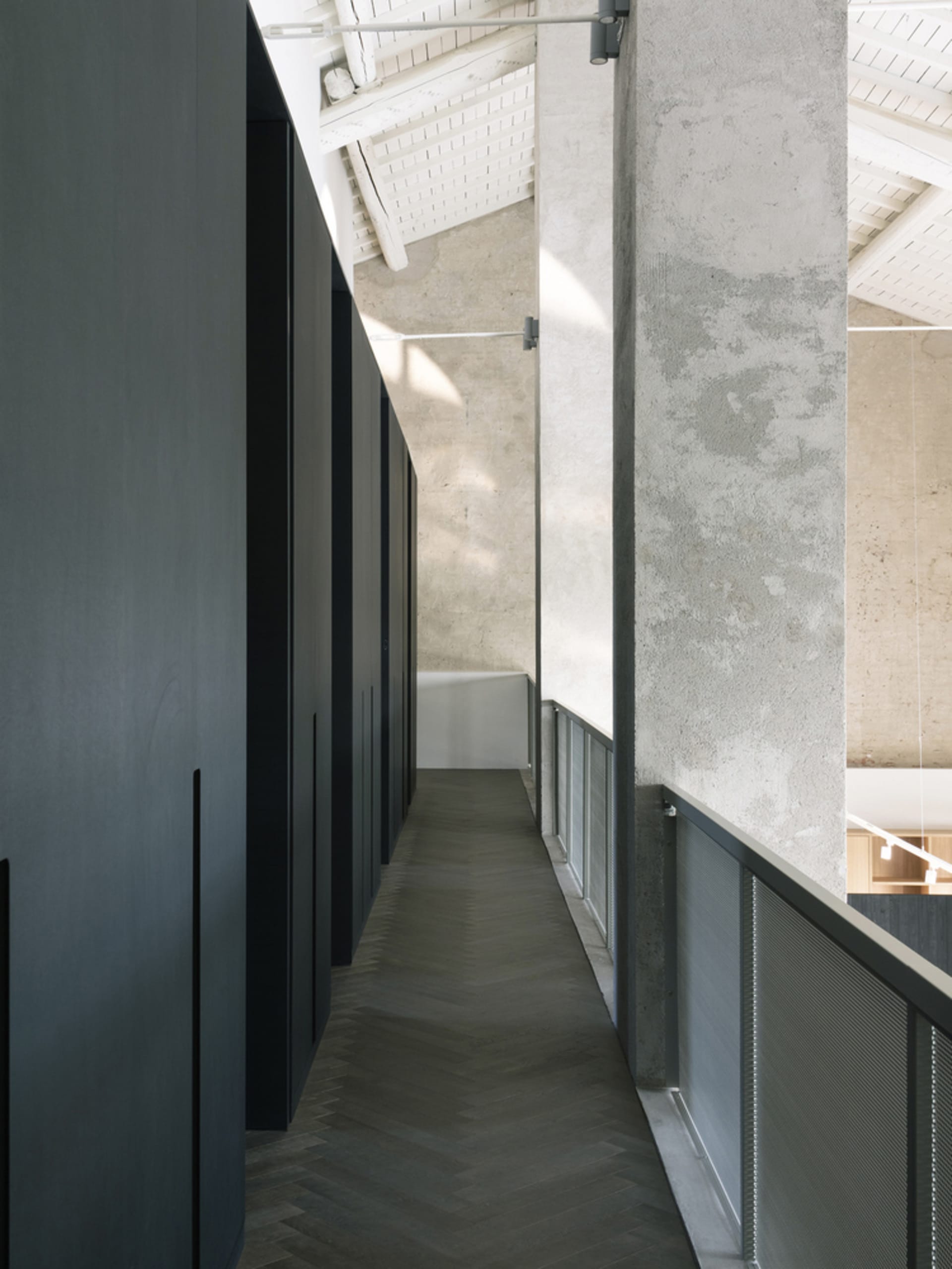 Modern industrial office hallway with concrete walls, herringbone wood floor, and concrete ceiling beams.