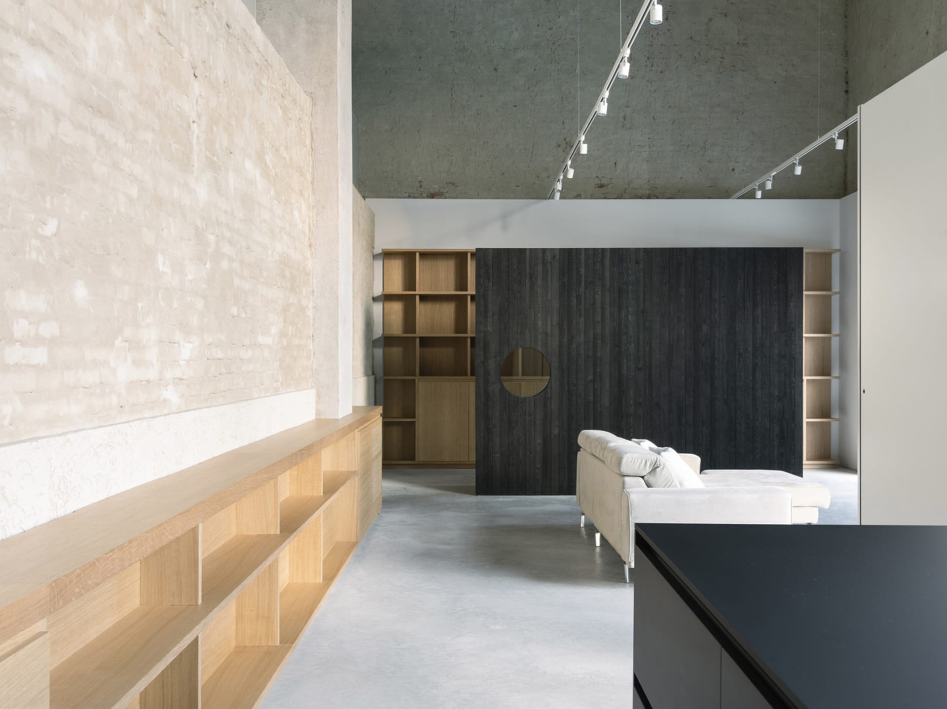A minimalist living room with concrete floors, wooden shelves, and metal accents, featuring a white sofa and a dark wooden wa