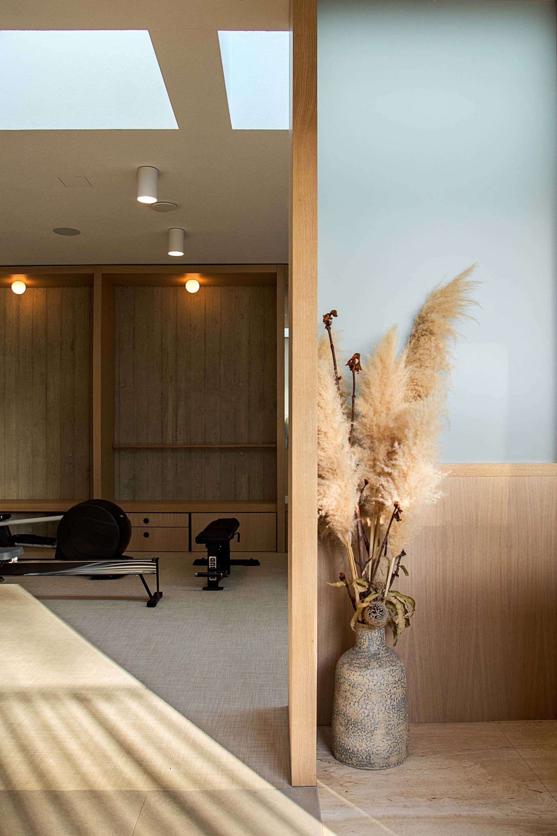 A minimalist fitness room with wood paneling, featuring exercise equipment and a vase of dried grasses.